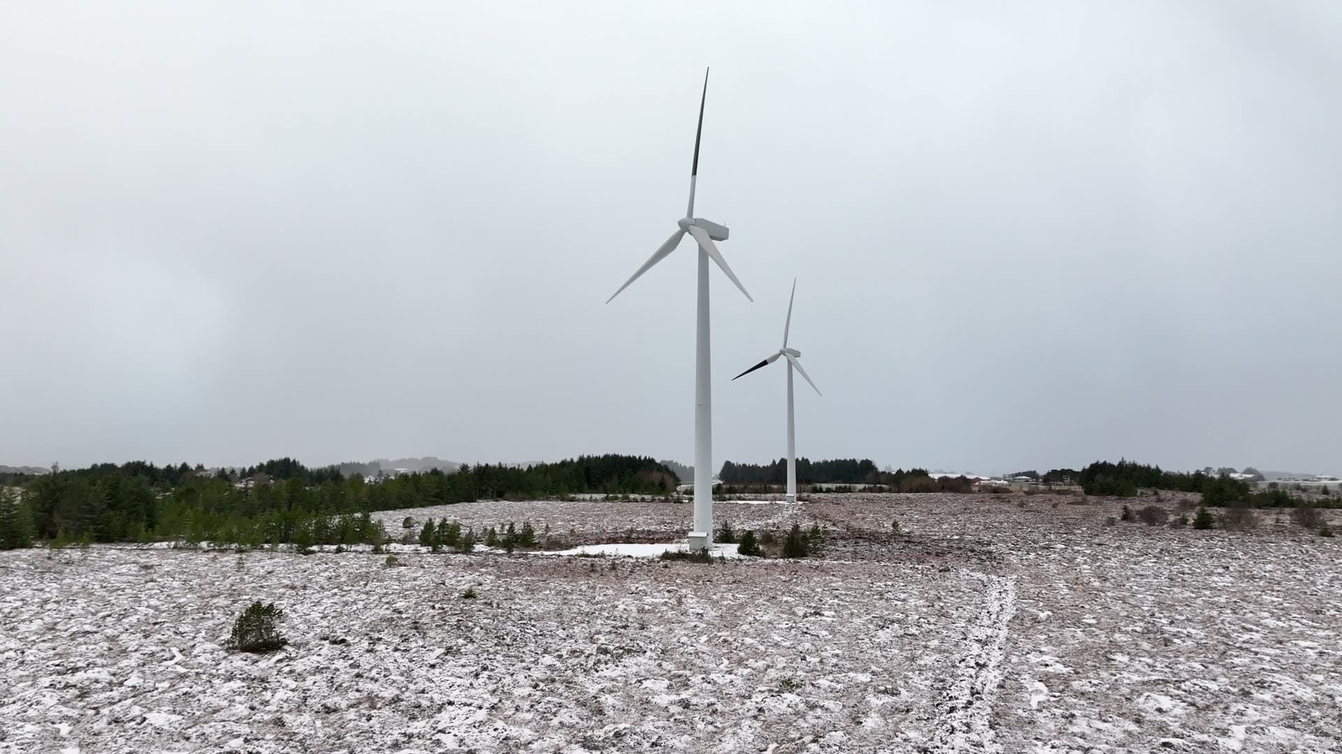 Two wind turbines turning over lightly snow covered ground, Harøy