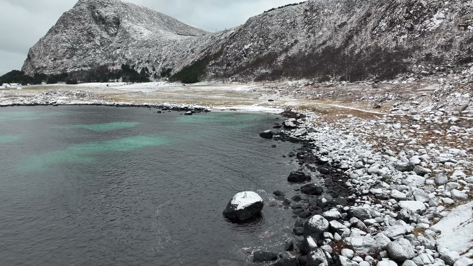 Snowy breakwater beside turquoise coastal water at Ulla