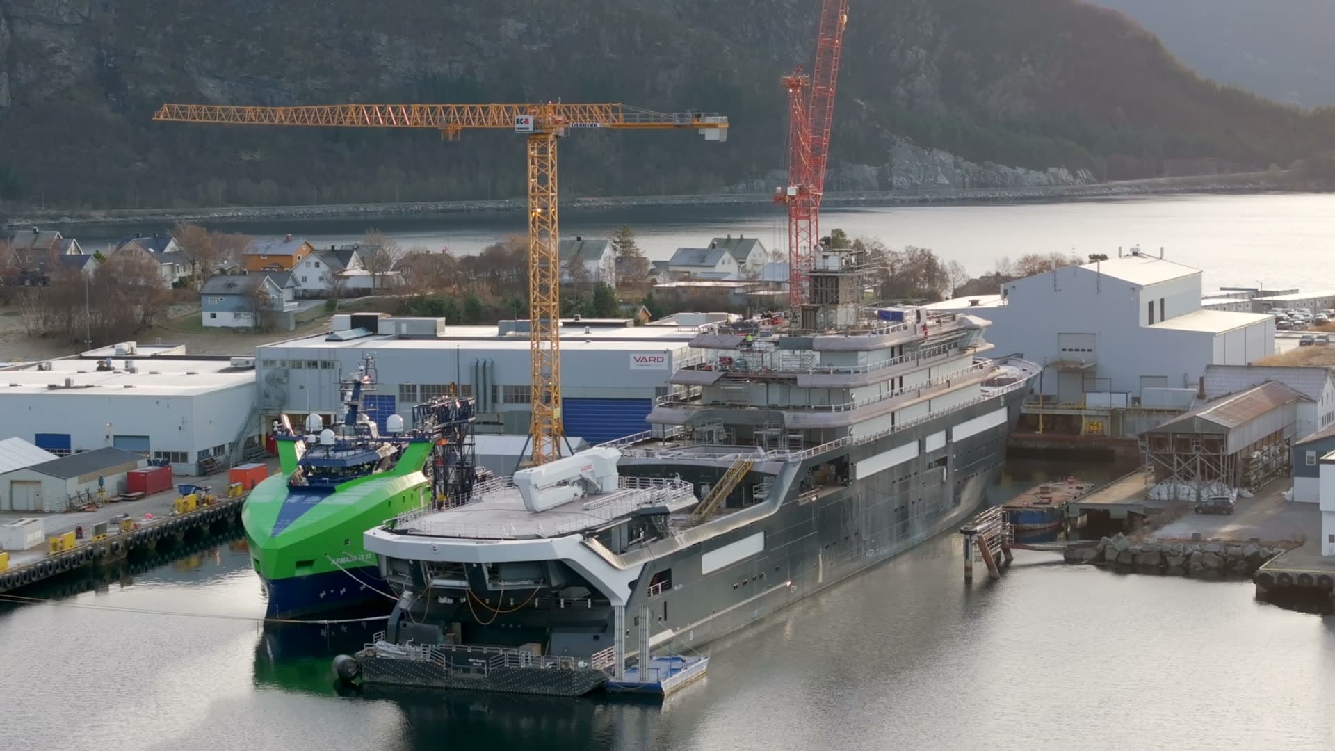 Aerial view of REV Ocean and a green vessel beside shipyard cranes
