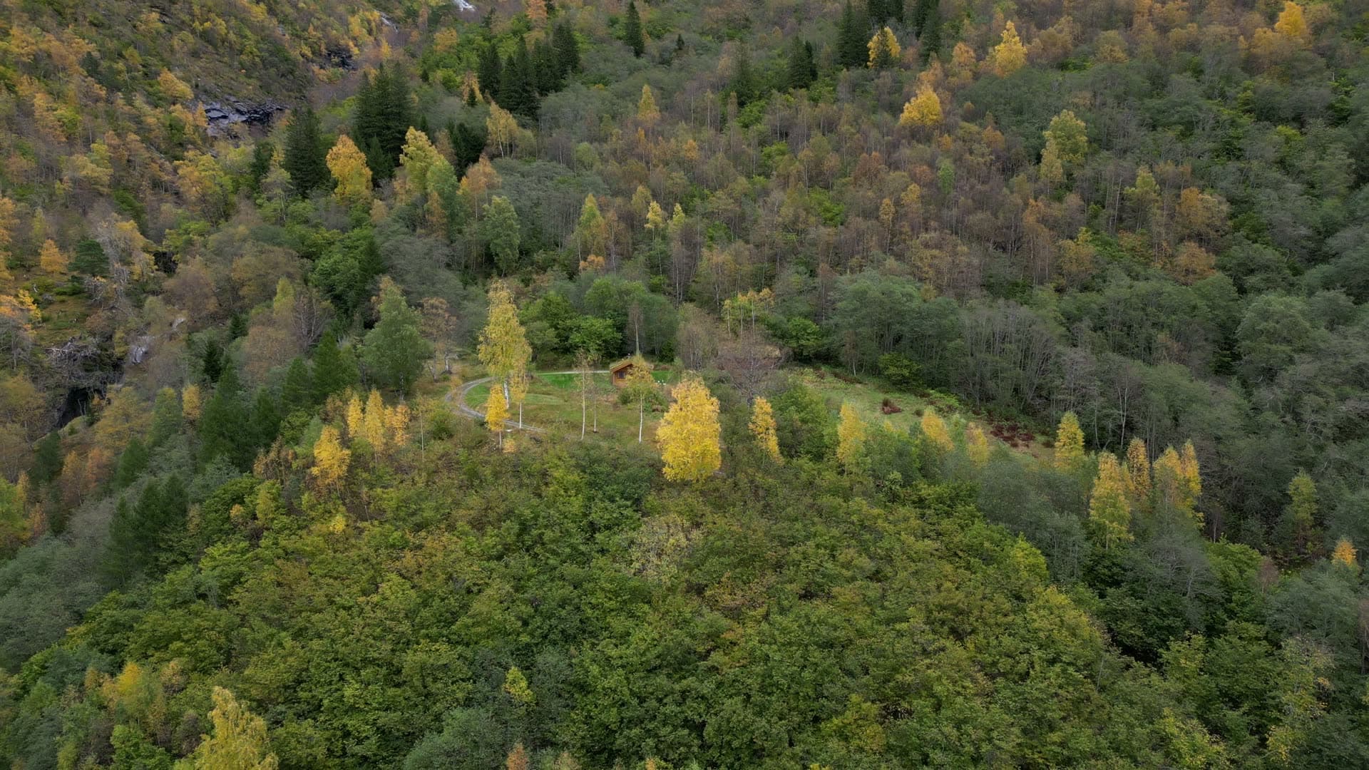 Cabin, fields and stream beneath mountains at Vike