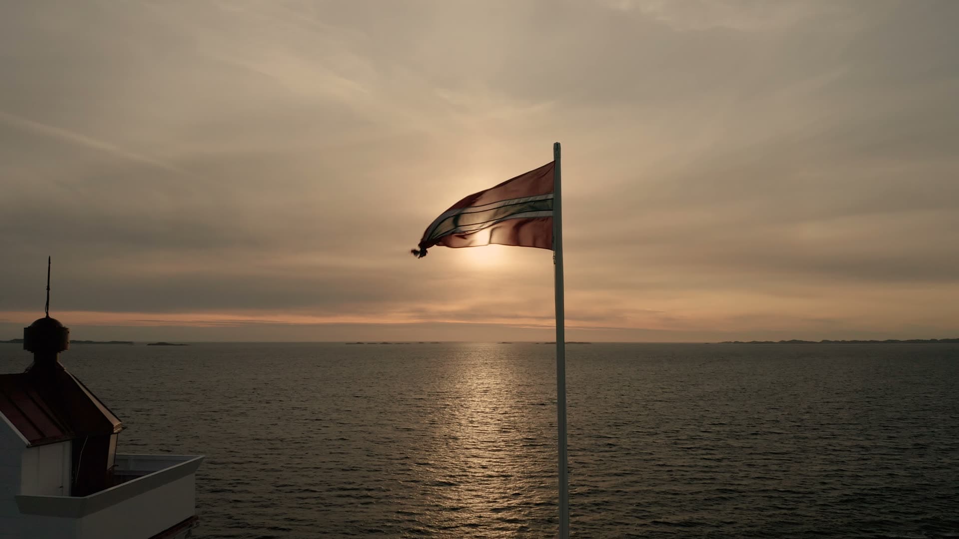 Norwegian flag waving at coastal sunset, Ryvarden fyr