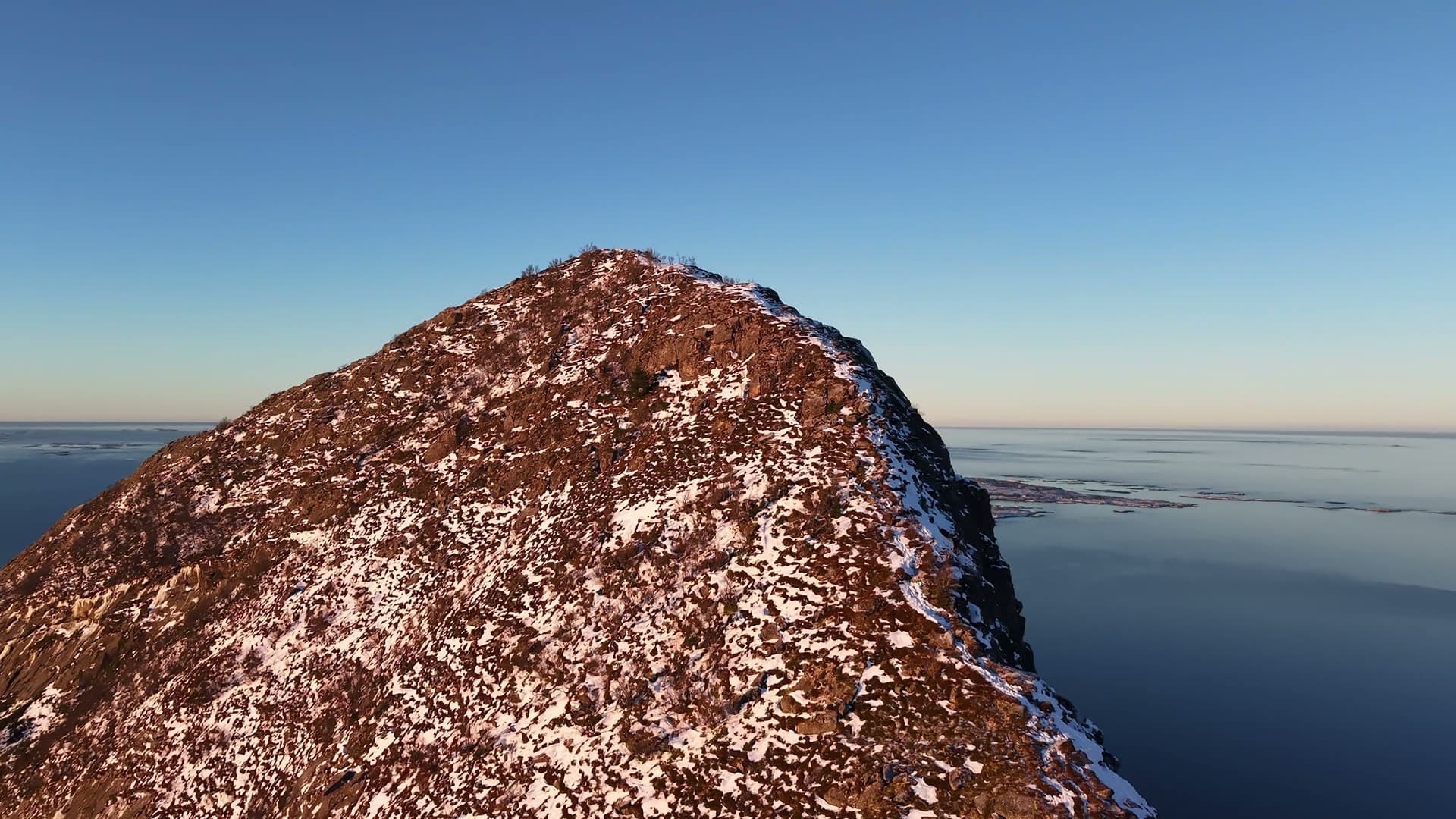 Snow-covered mountain peak over frozen lake, Reipå