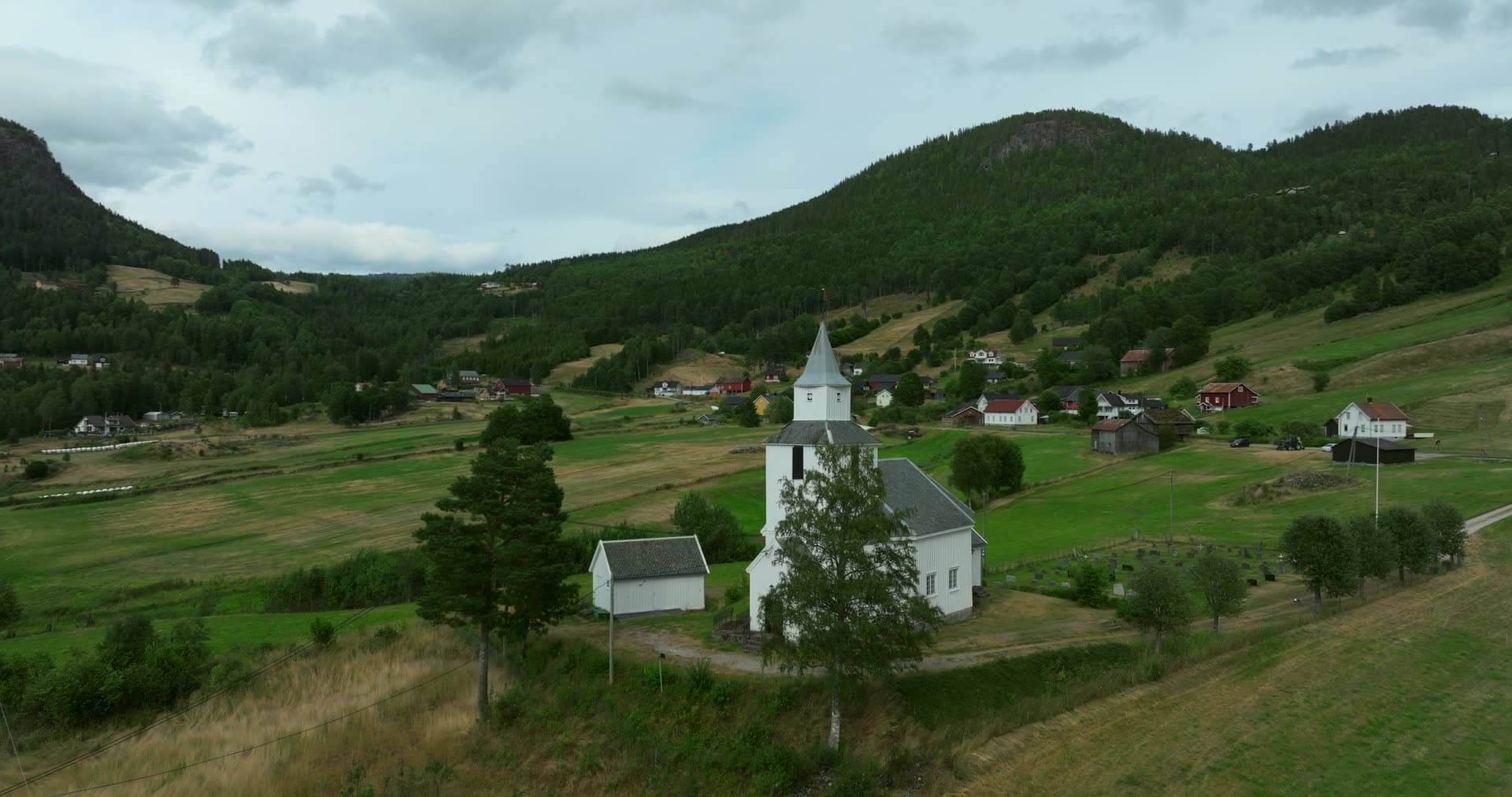 White wooden church on a hill above hay fields, Åraksbø, Norway