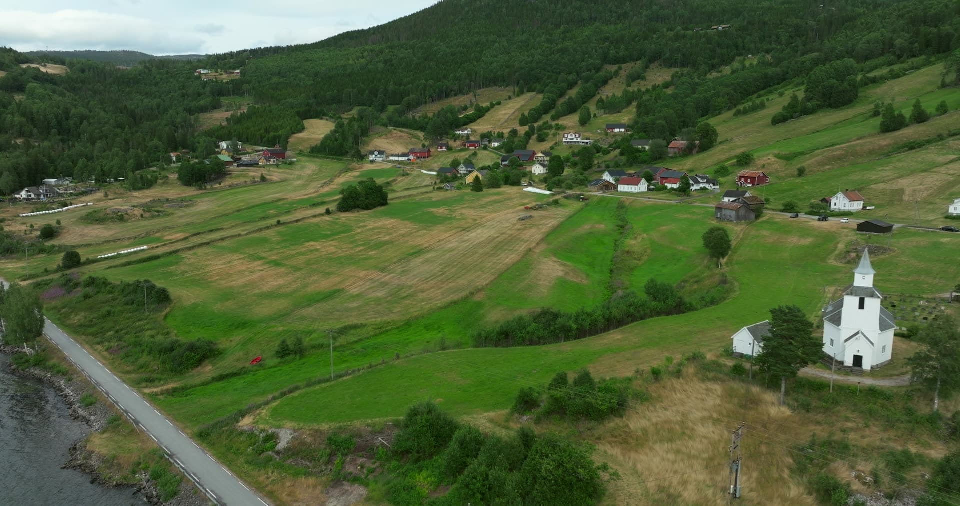 White church above mown hayfields by lake road, Åraksbø, Norway