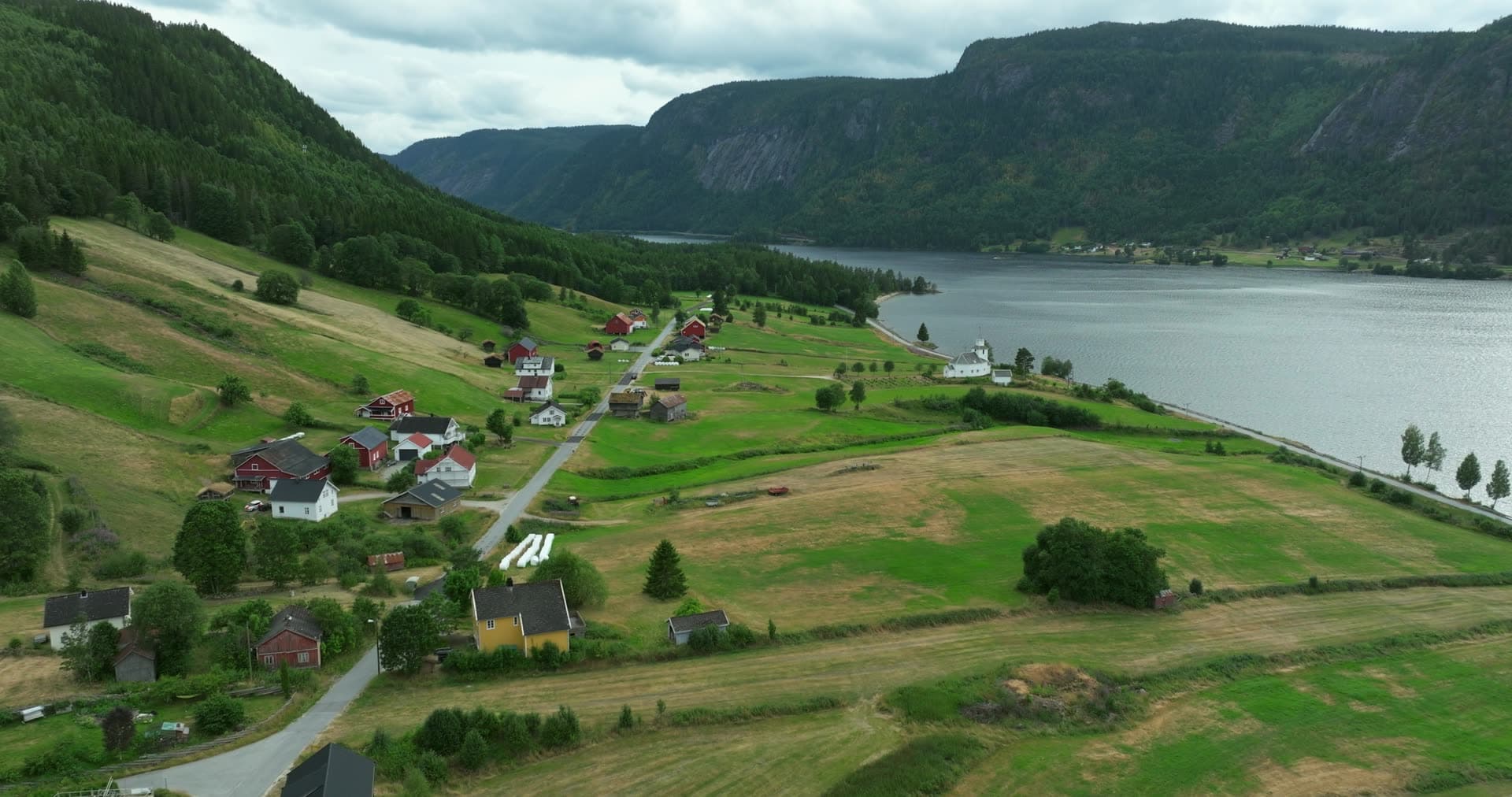 White church and farms on hayfields by the lake, Åraksbø, Norway