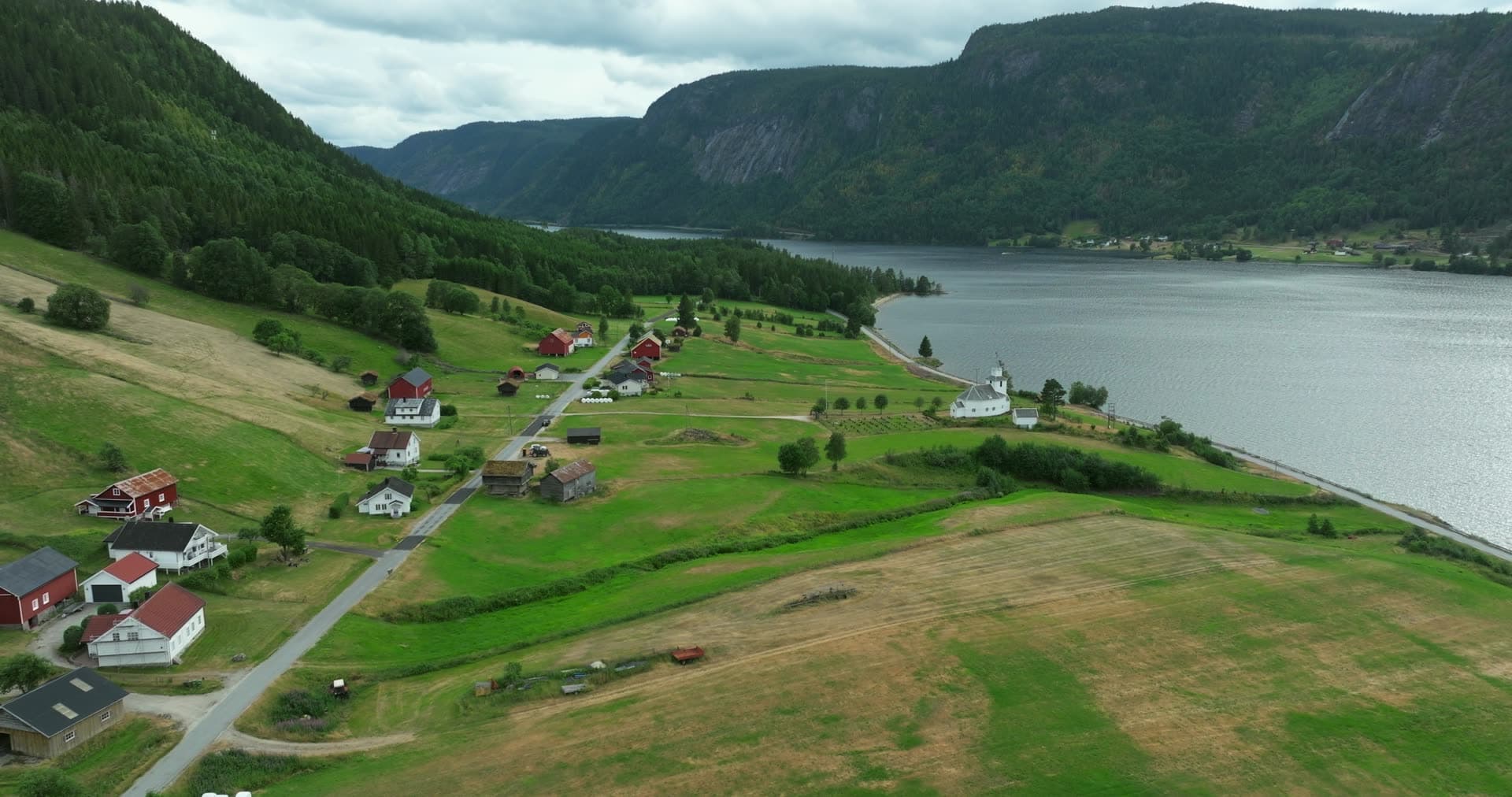 White church and red farms on lakeside fields, Åraksbø, Norway