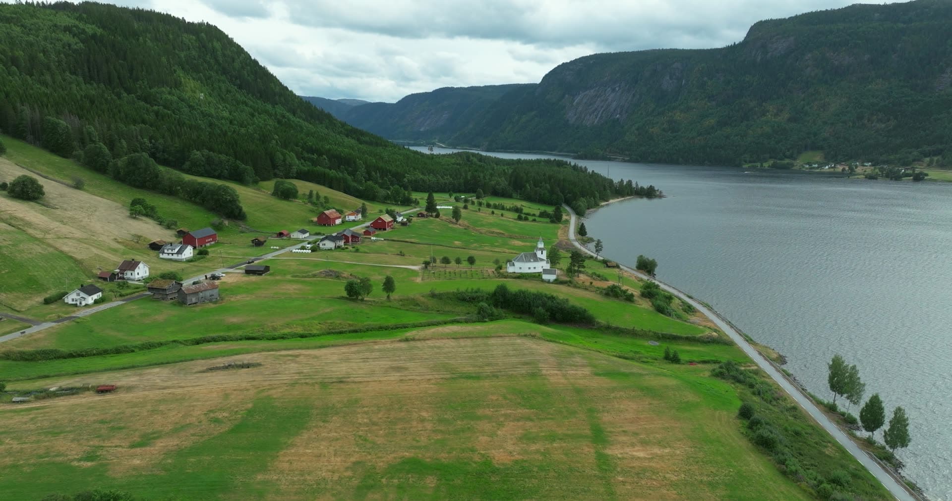 White church and red farms by lakeside fields, Åraksbø, Norway