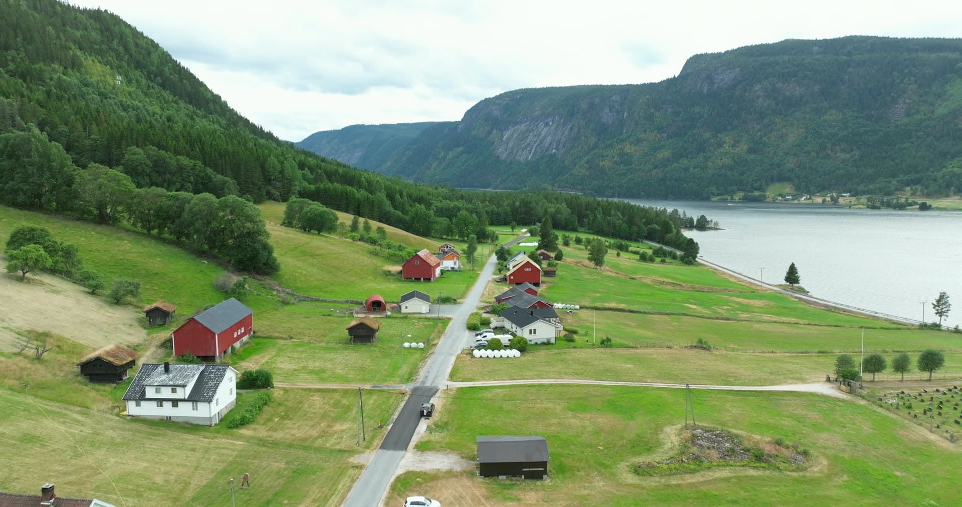 Red barns and tractors along lakeside farm road, Åraksbø, Norway
