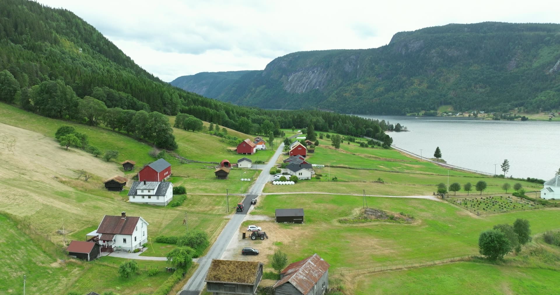 Farm road past red barns and white church by lake, Åraksbø, Norway