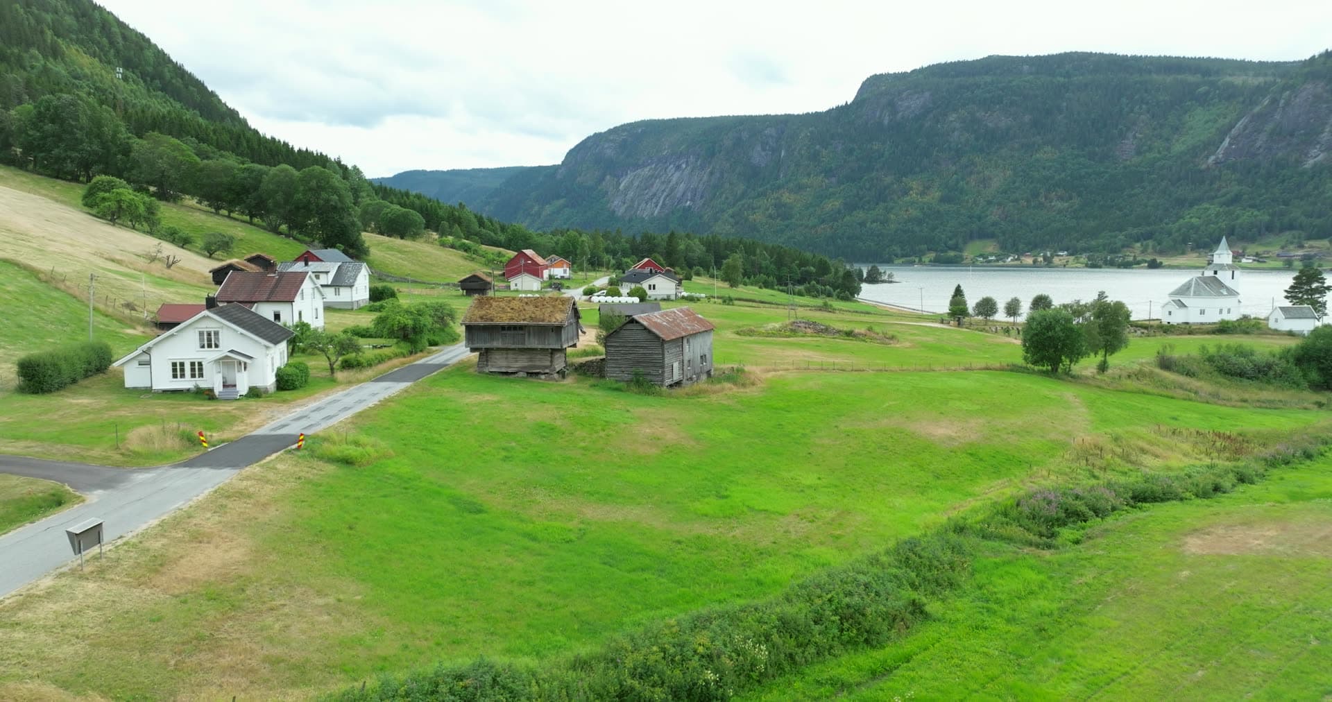 Turf-roofed barns and white church by the lake, Åraksbø, Norway