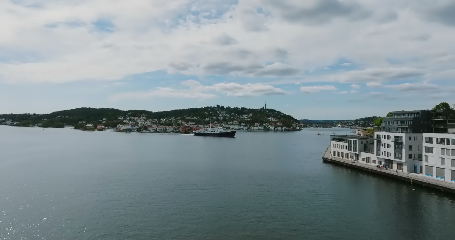 Cargo ship in the strait past white waterfront flats, Arendal, Norway