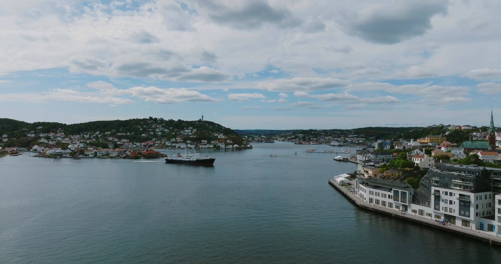 Dark cargo ship passing white waterfront blocks, Arendal, Norway