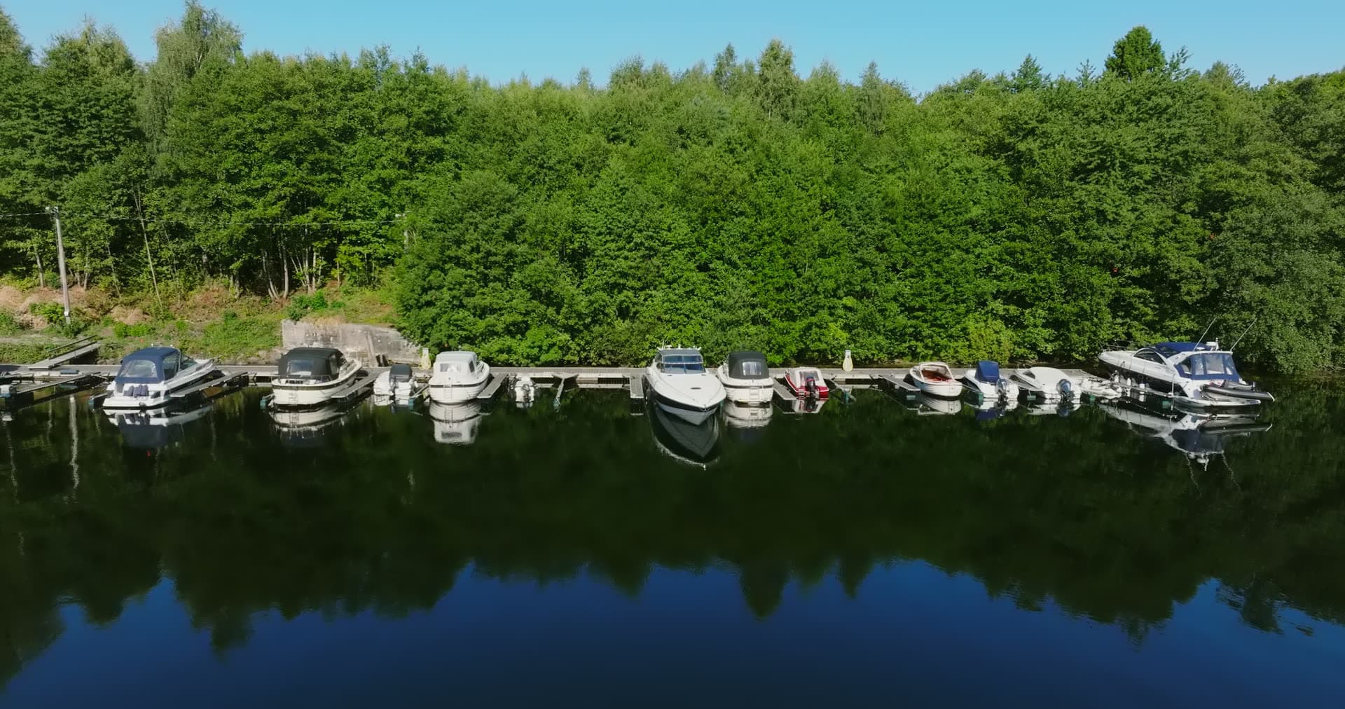 Motorboats at dock below wooded bank, Bomsholmen, Norway