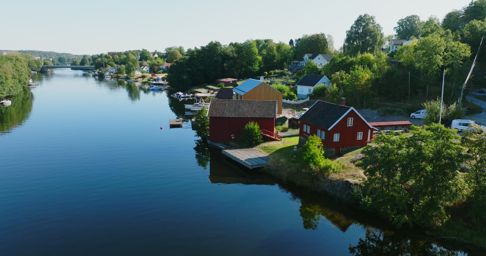Red boathouse and dock on calm river, Bomsholmen, Norway