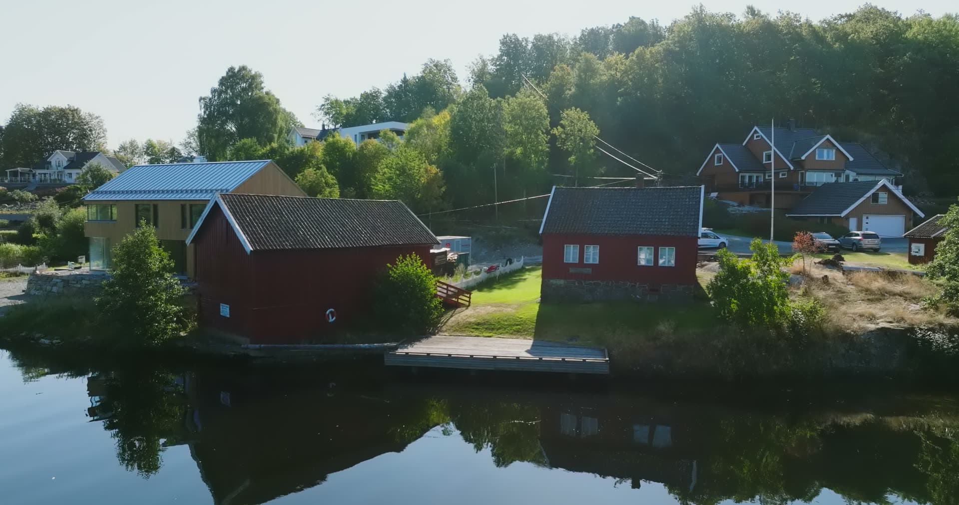 Red boathouses and dock on still water, Bomsholmen, Norway