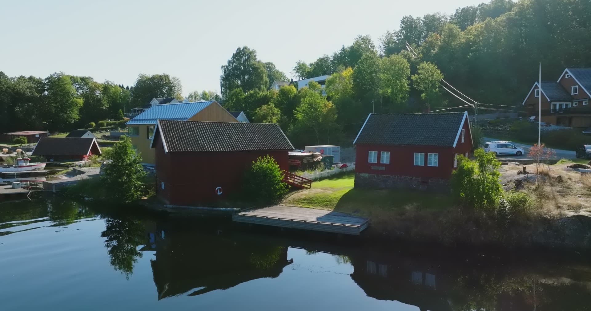 Red boathouses and jetty on still water, Bomsholmen, Norway