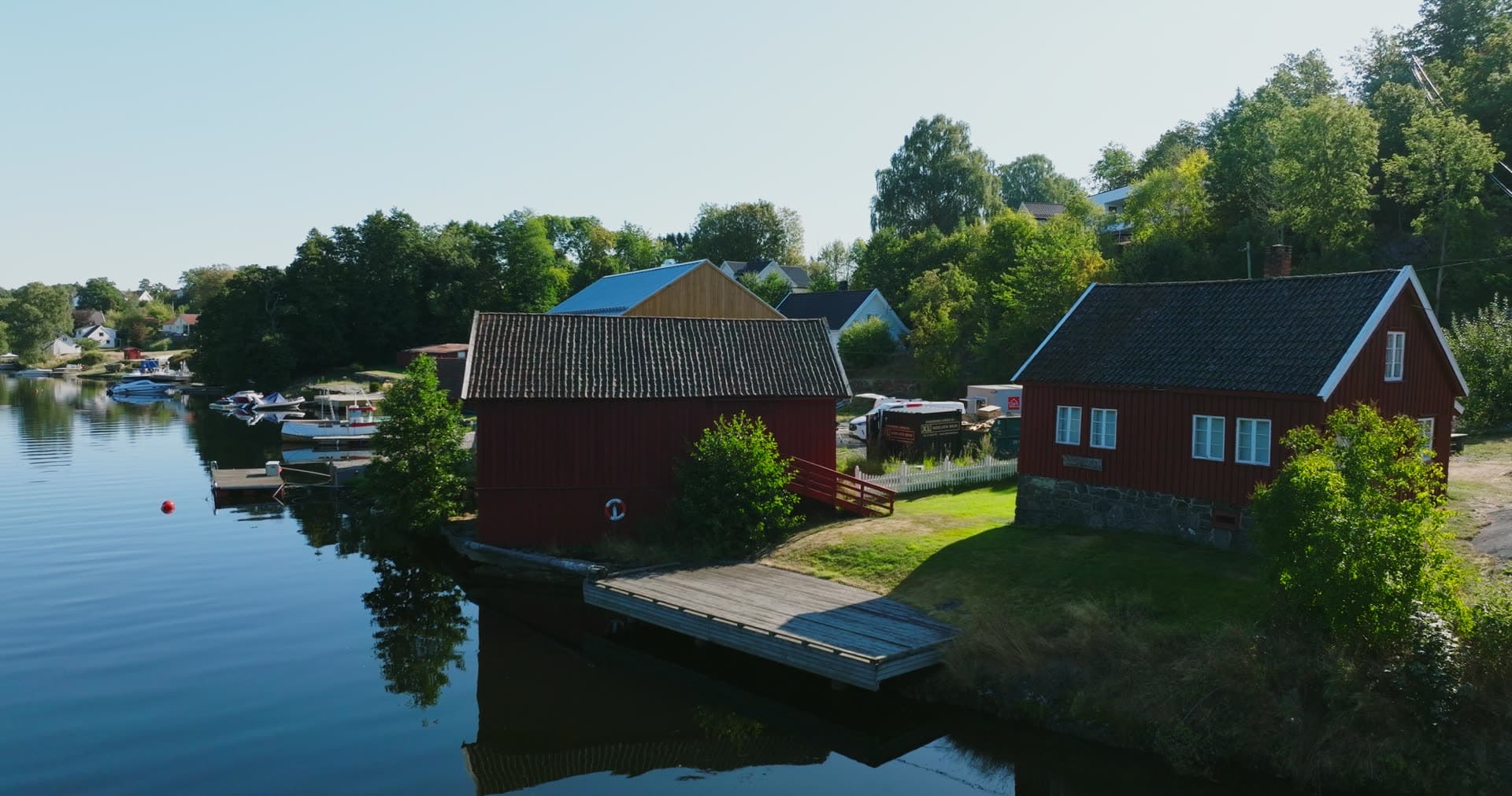 Red boathouse and wooden dock on still inlet, Bomsholmen, Norway
