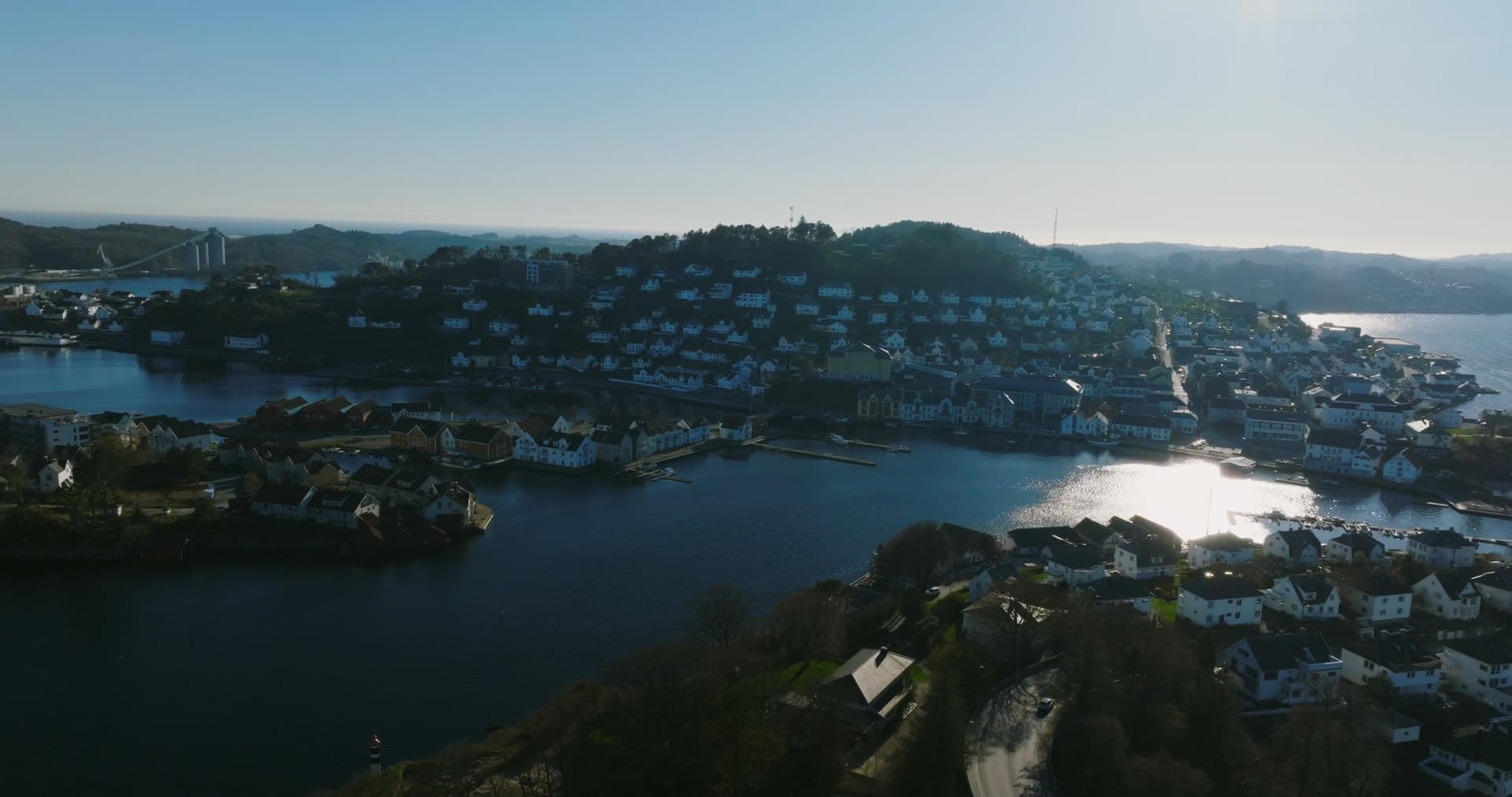Sun glare on inlet by white hillside town, Farsund, Norway