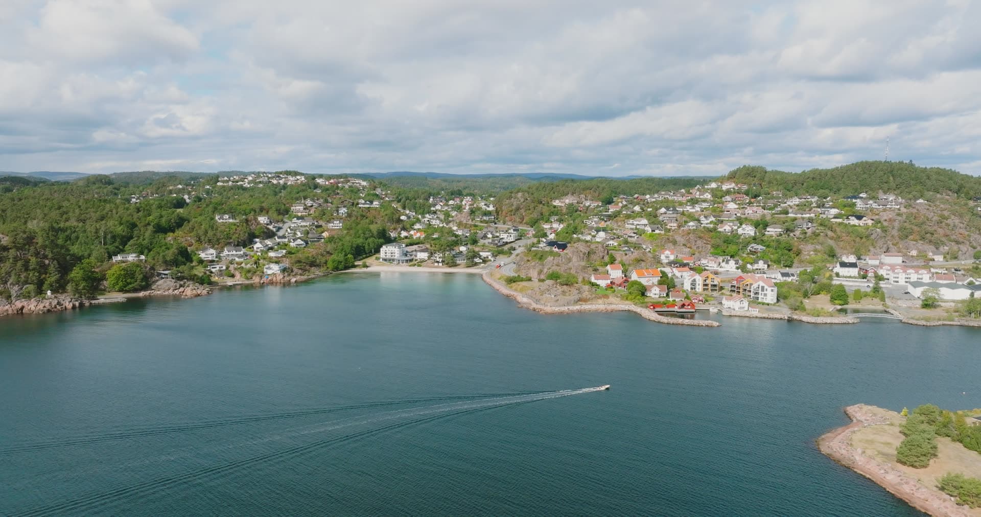 Boat wake crossing bay off hillside houses, Fevik, Norway