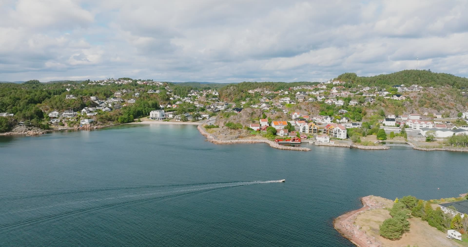 Motorboat wake past hillside houses and beach, Fevik, Norway