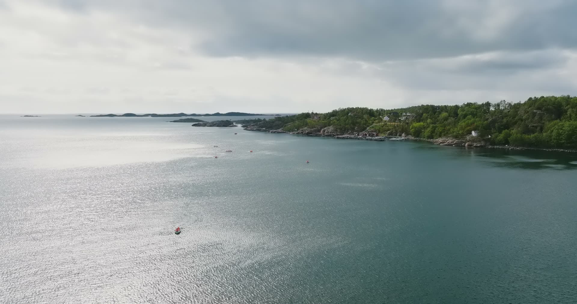 Small boat crossing bay off wooded shore, Fevik, Norway