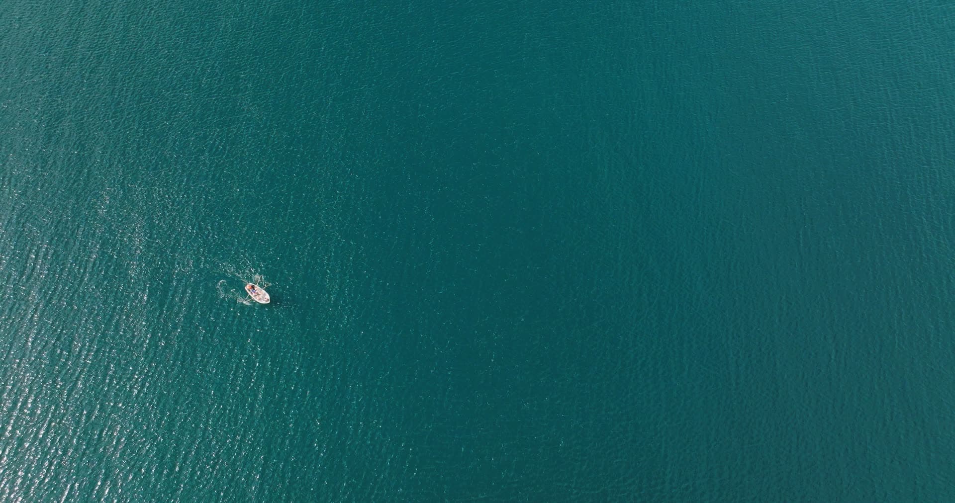 Small white boat alone on open teal sea, Fevik, Norway