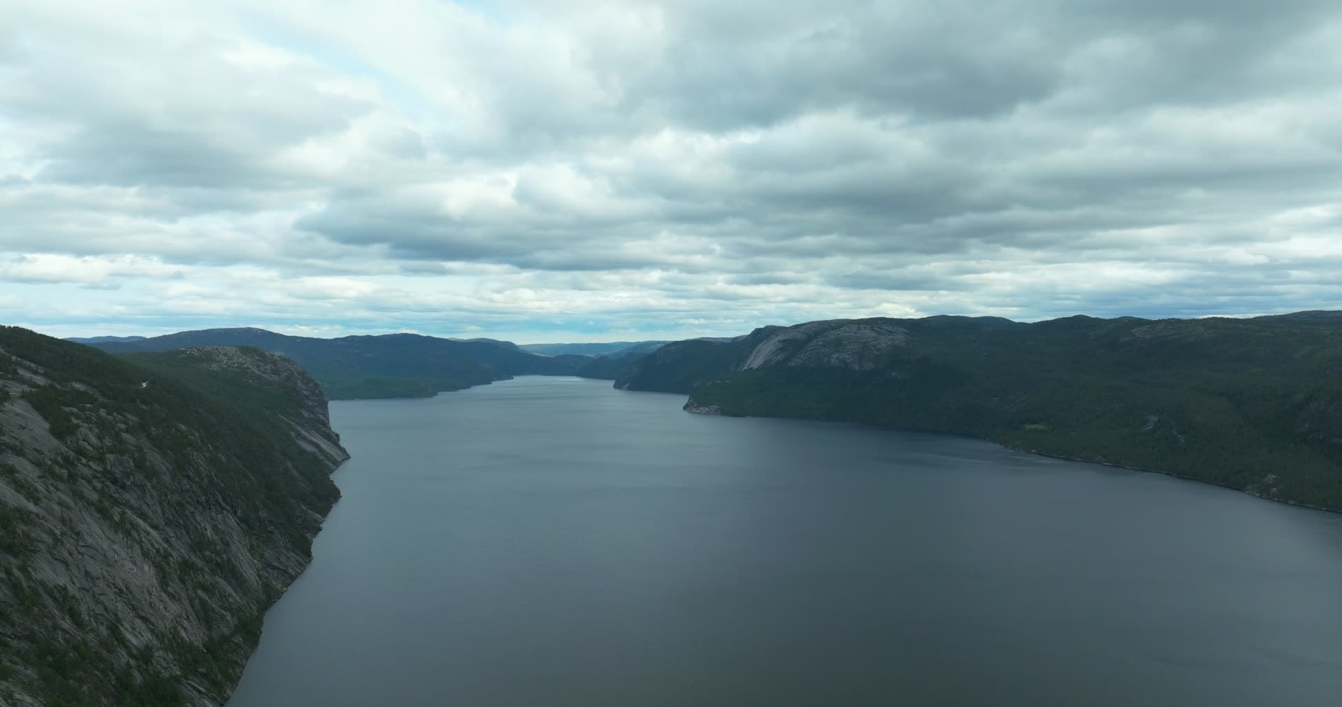 Steep cliff face above long lake under grey clouds, Fyresdal, Norway