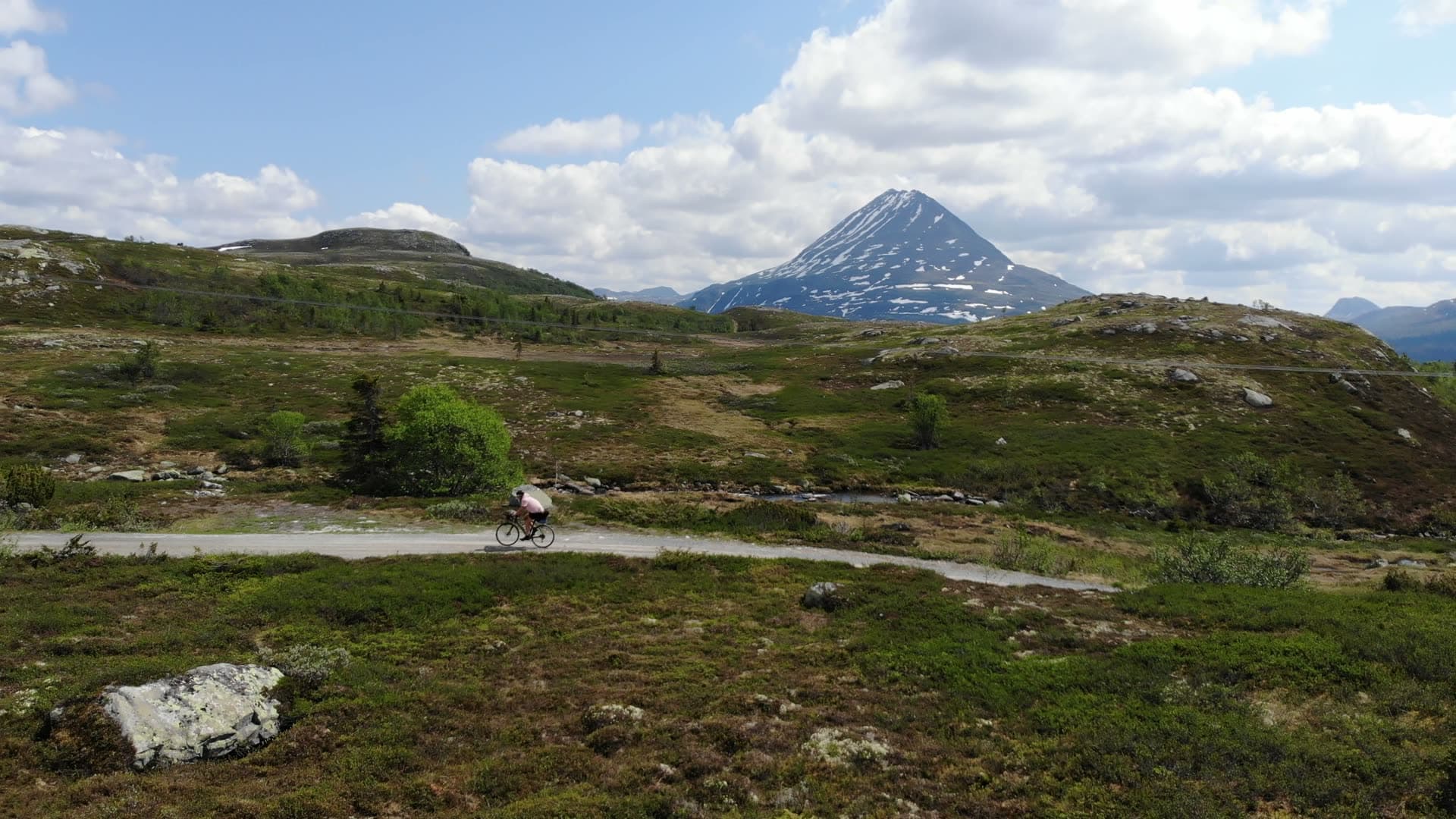 Cyclist on gravel road below snowy peak, Gaustatoppen, Norway