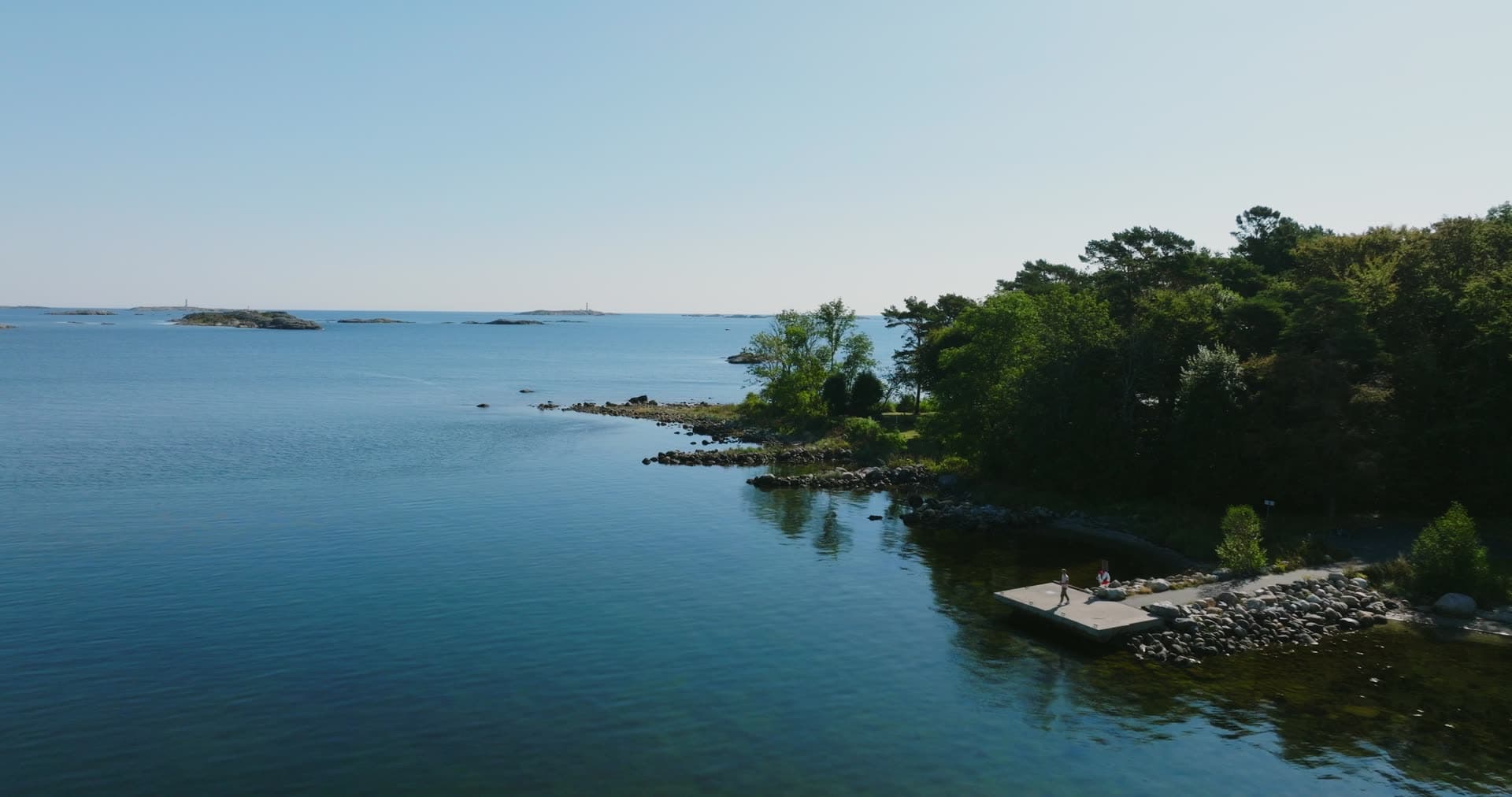 Two people on concrete jetty by wooded shore, Hasseltangen, Norway