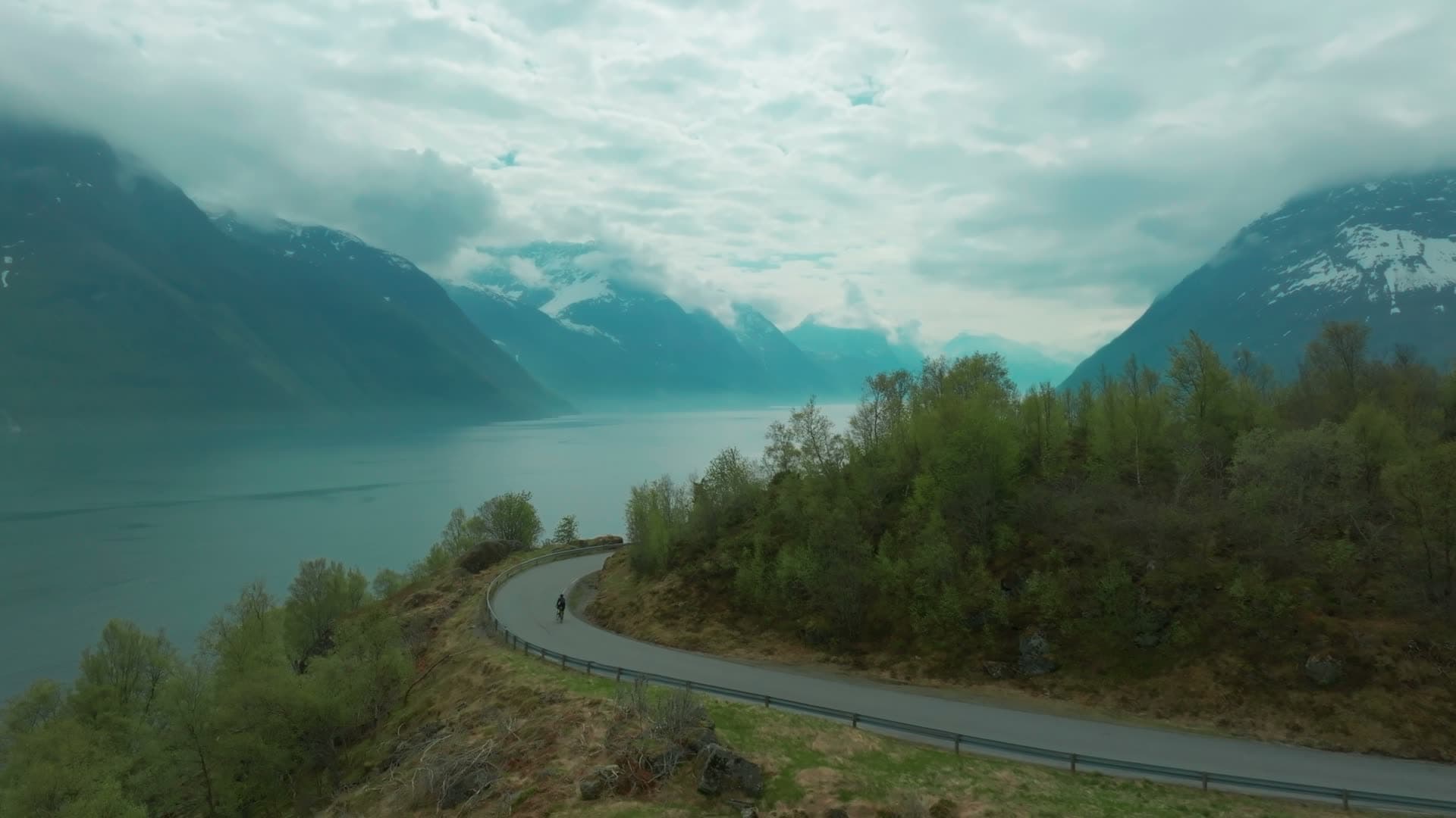 Cyclist on curving road above the fjord, Hjørundfjorden, Norway