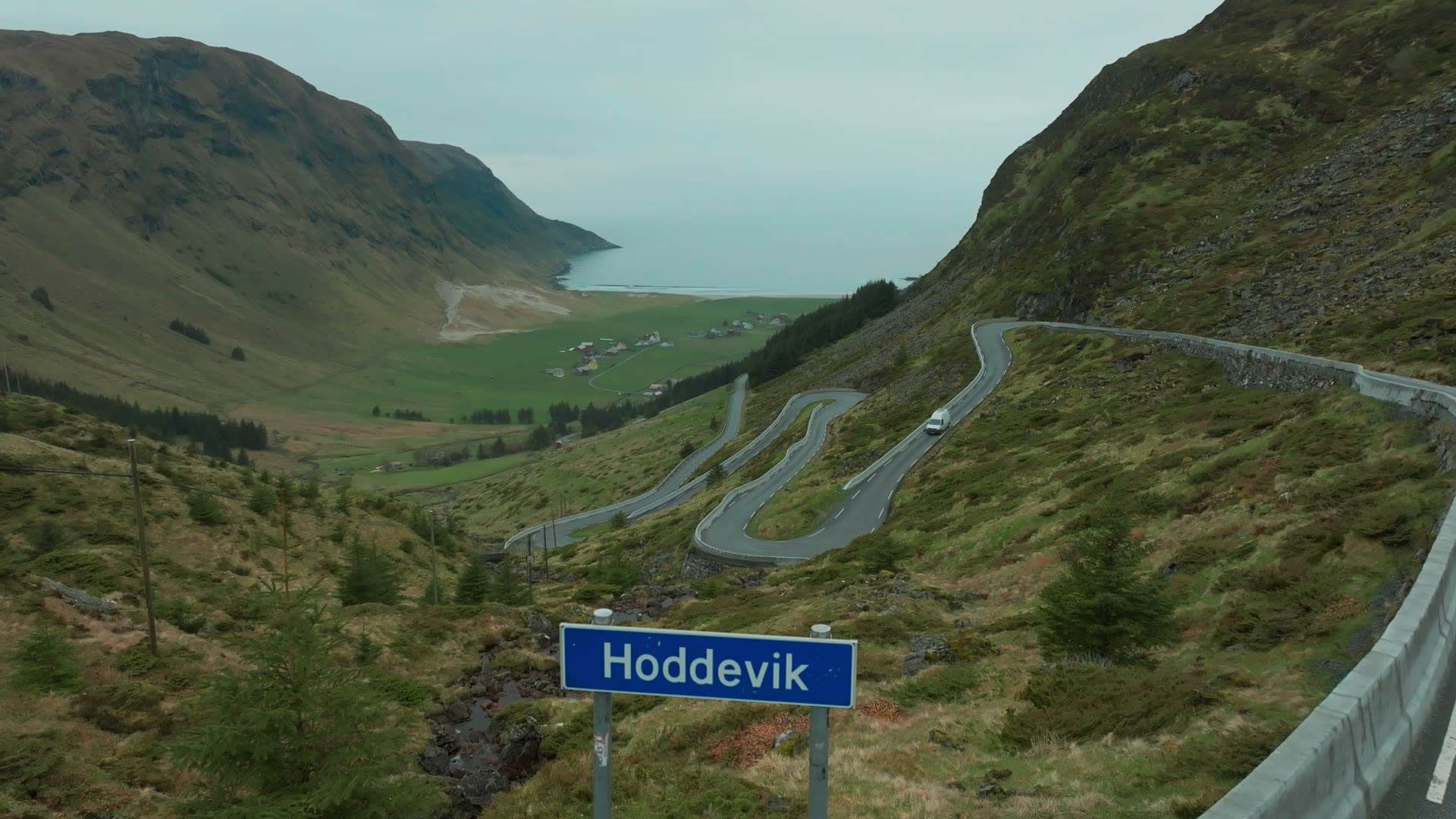 White van on hairpin road above blue road sign, Hoddevik, Norway