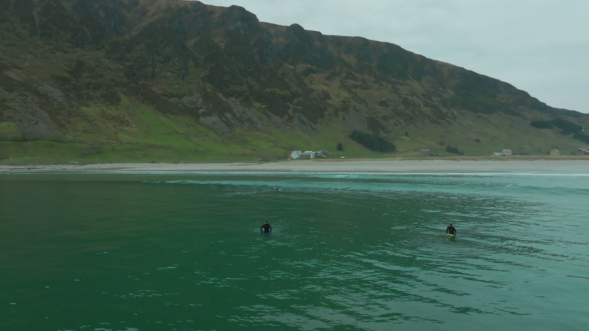 Surfers waiting on green water off beach, Hoddevik, Norway