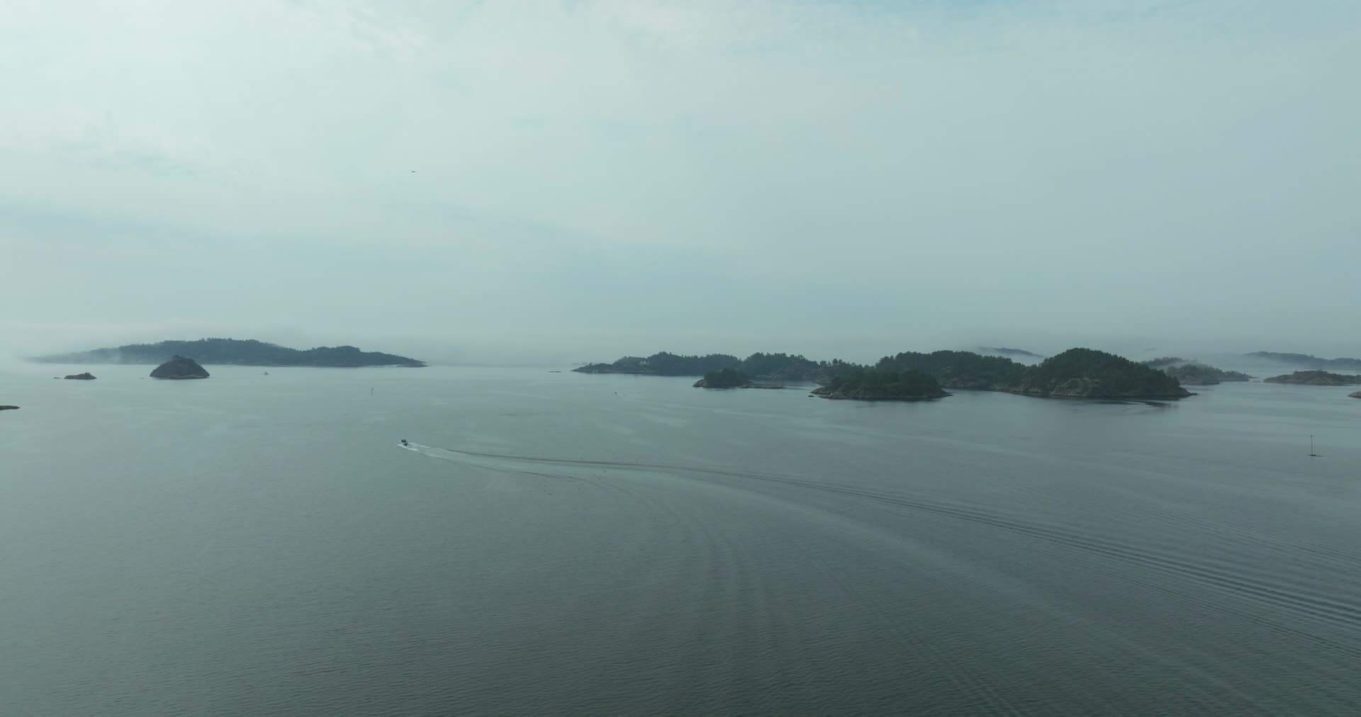 Small boat trailing wake past hazy islets, Høllen, Norway