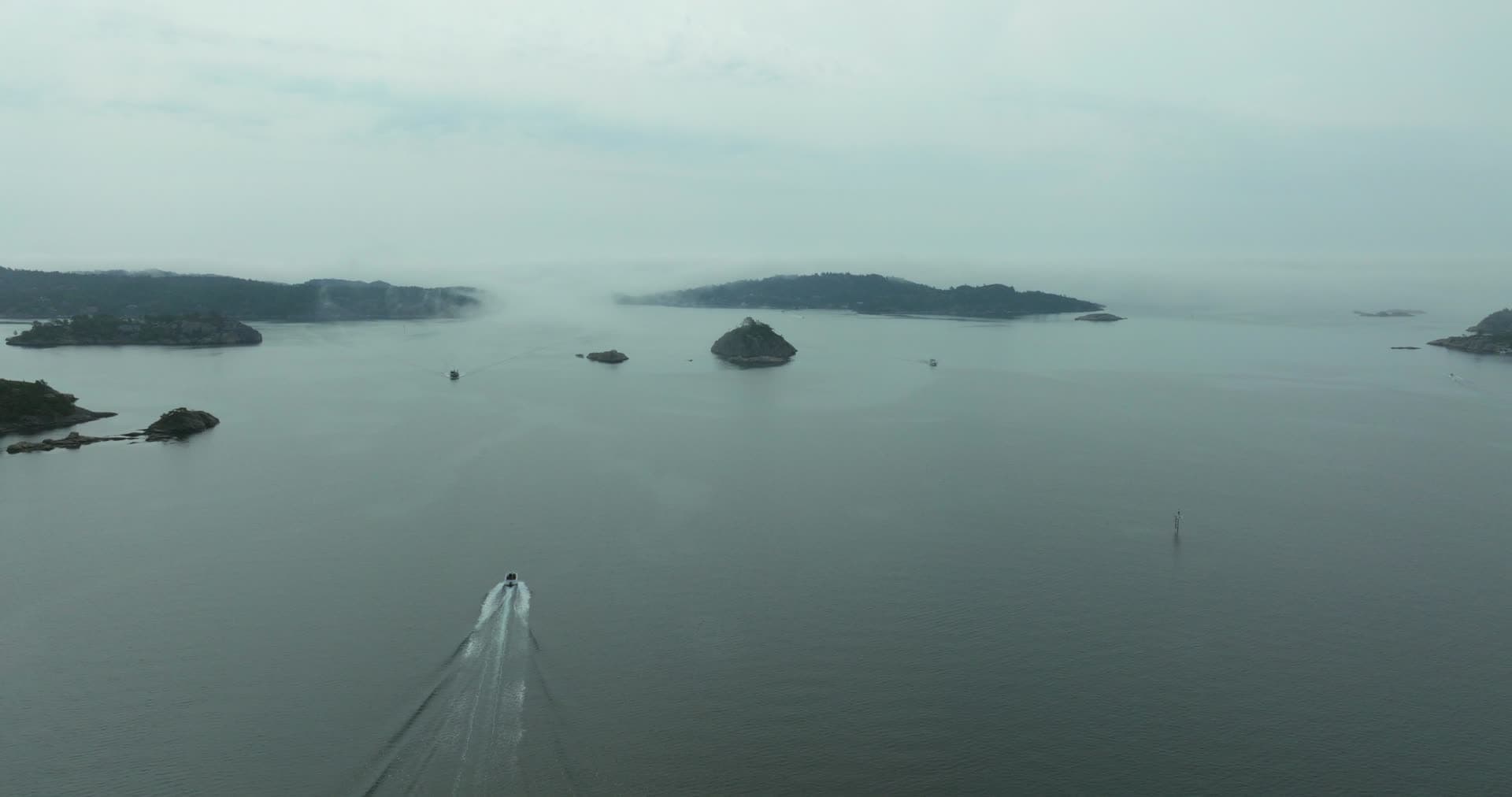 Speedboat wake past a rock islet in fog, Høllen, Norway