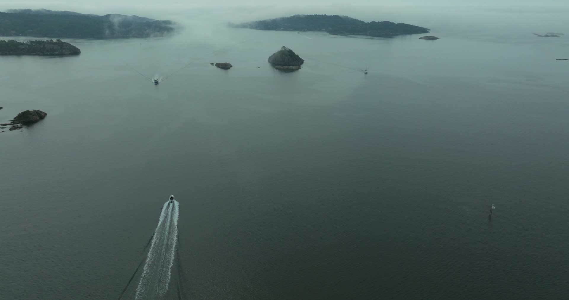Speedboat wake past rocky islets in fog, Høllen, Norway