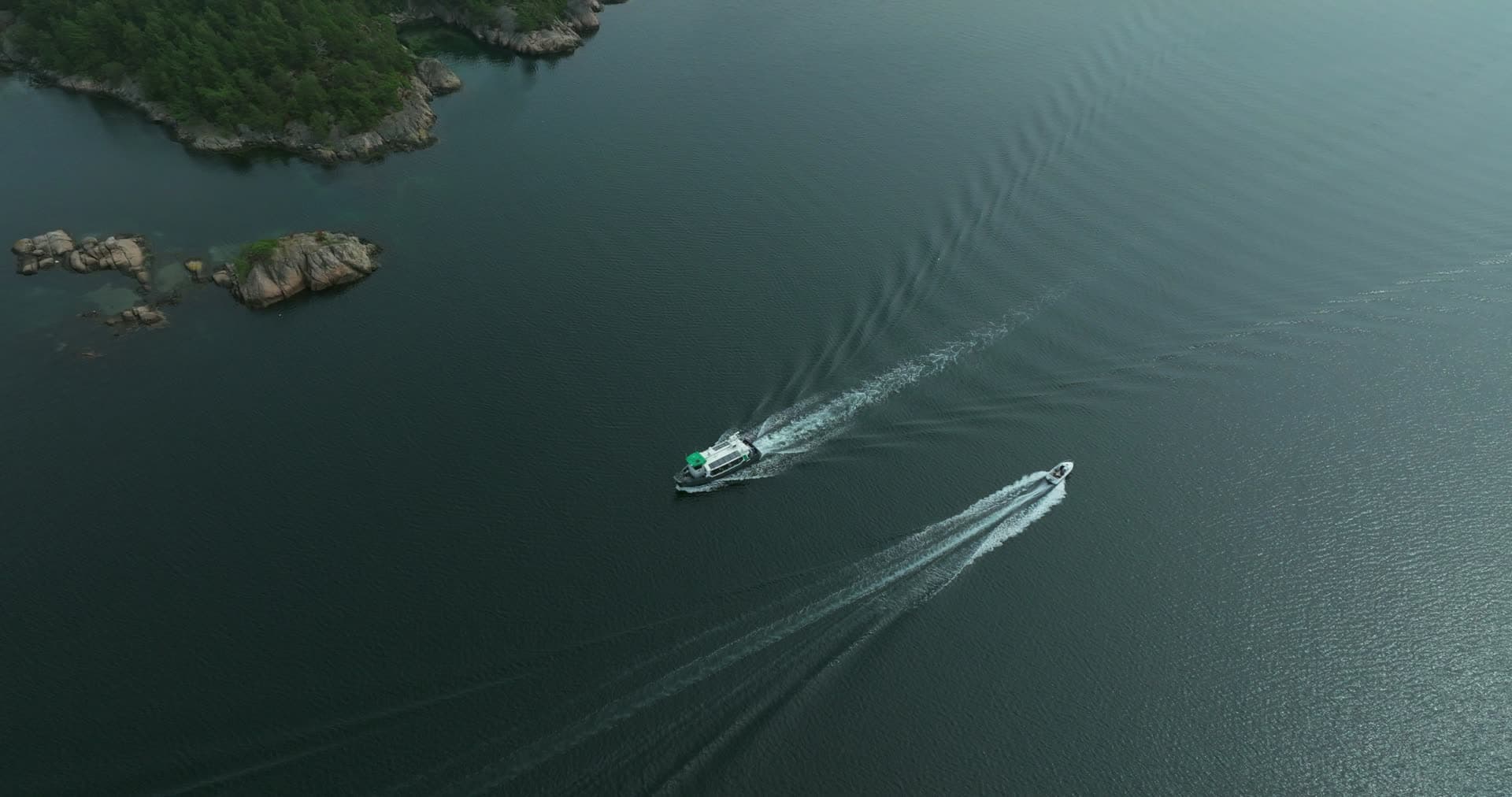 Two boats crossing wakes past rocky islets, Høllen, Norway