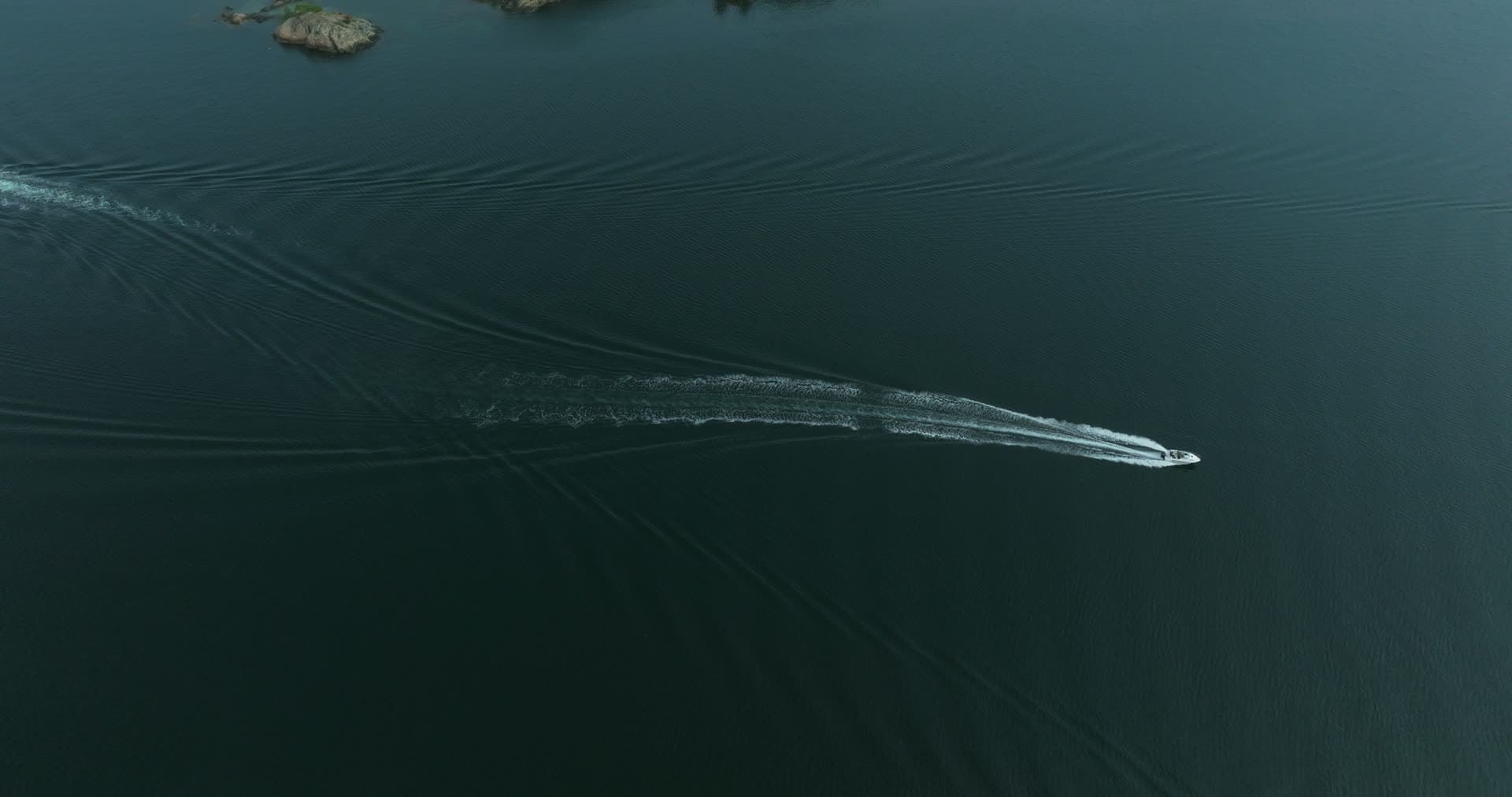 Speedboat carving a long wake past rocky islets, Høllen, Norway