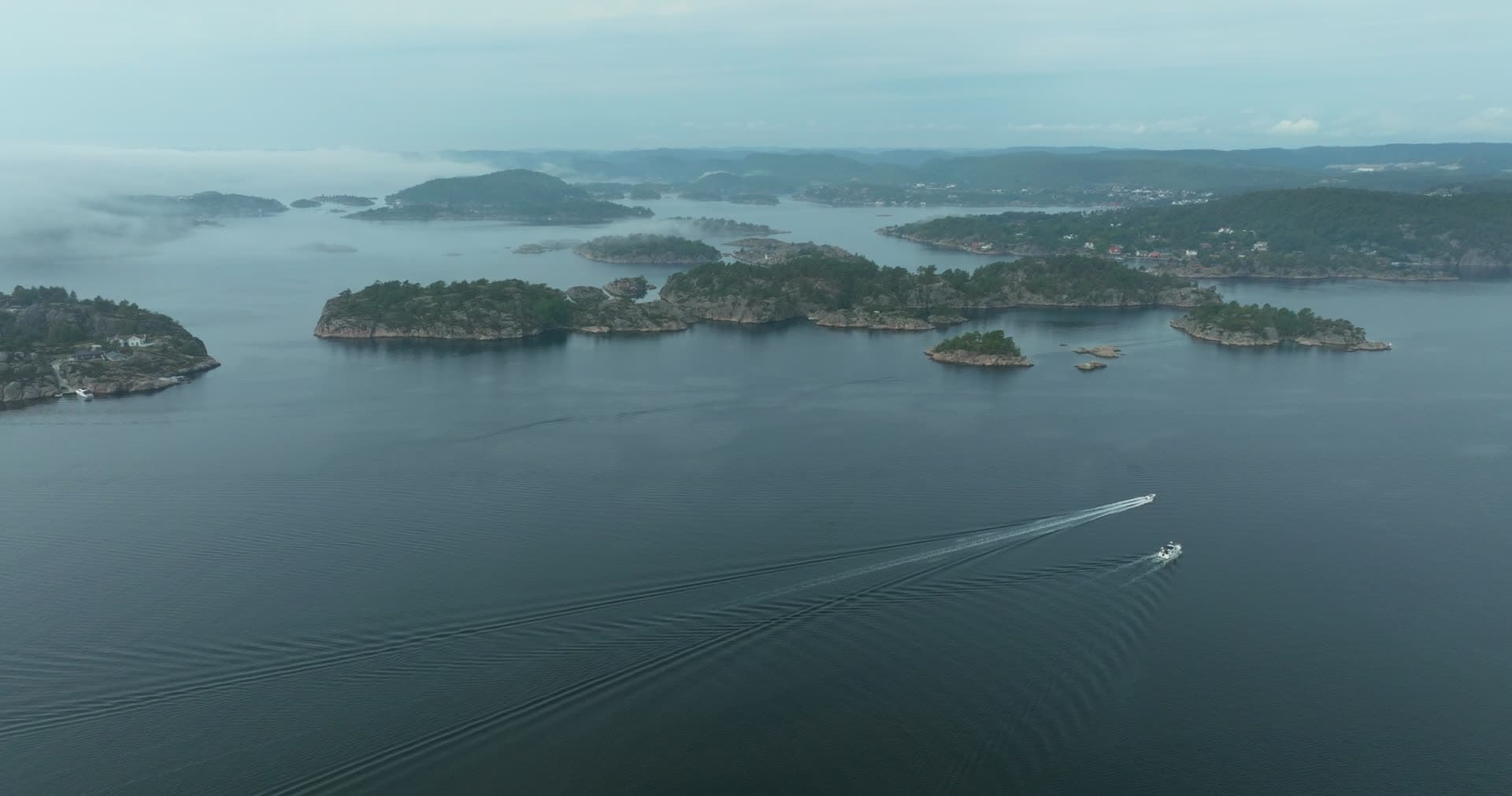 Motorboat wake between misty islets, Høllen, Norway