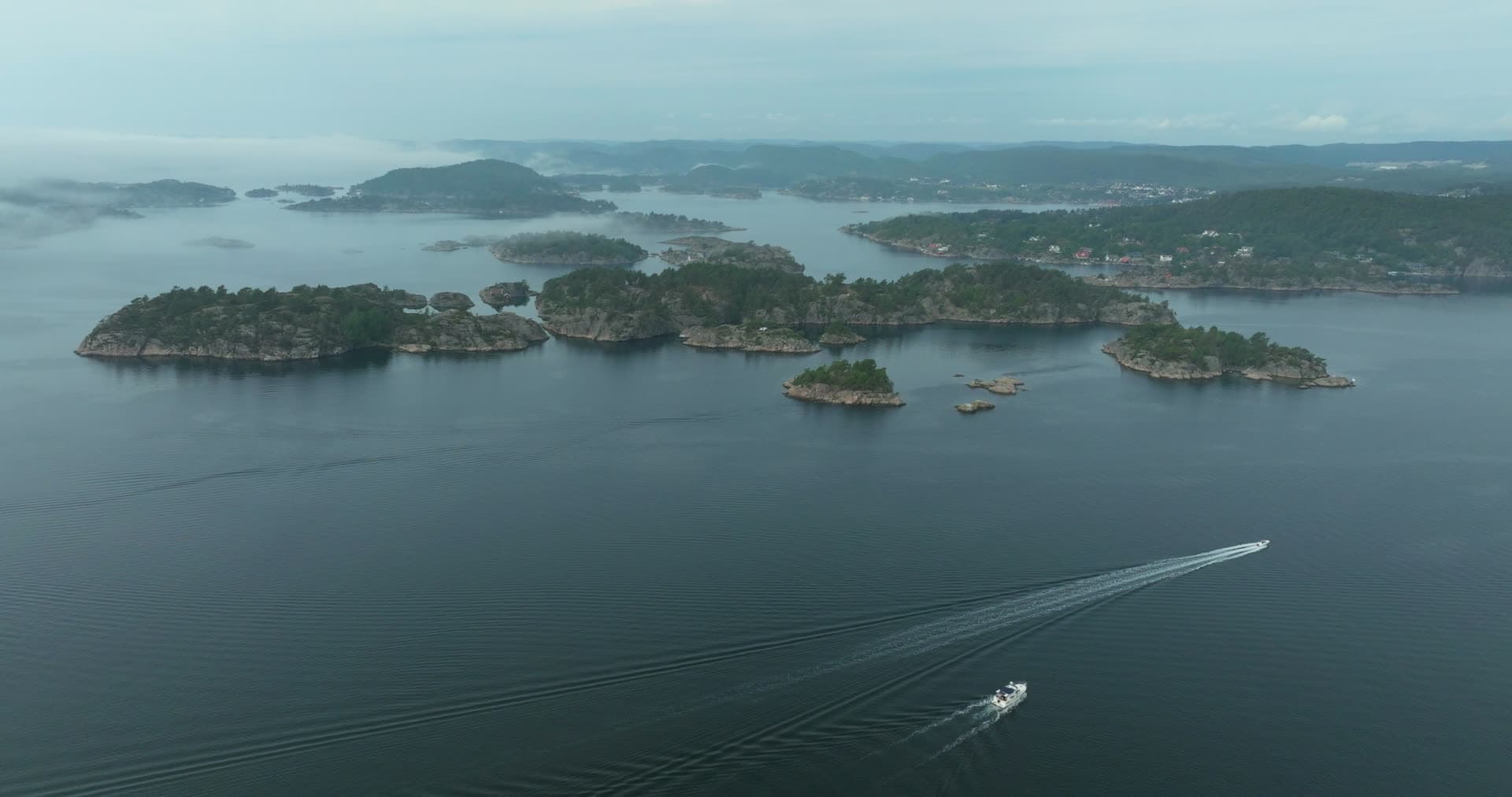 Motorboat trailing wake past wooded islets, Høllen, Norway