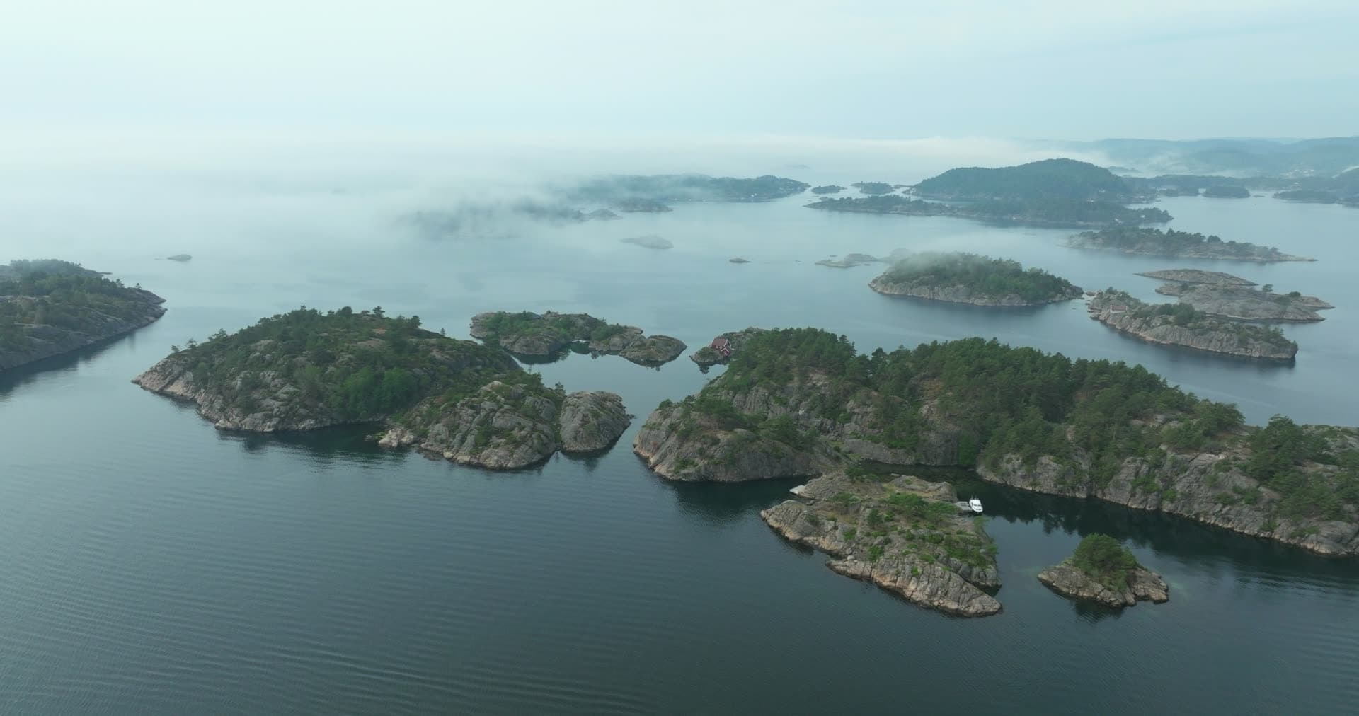 Fog over pine-topped skerries and red cabin, Høllen, Norway