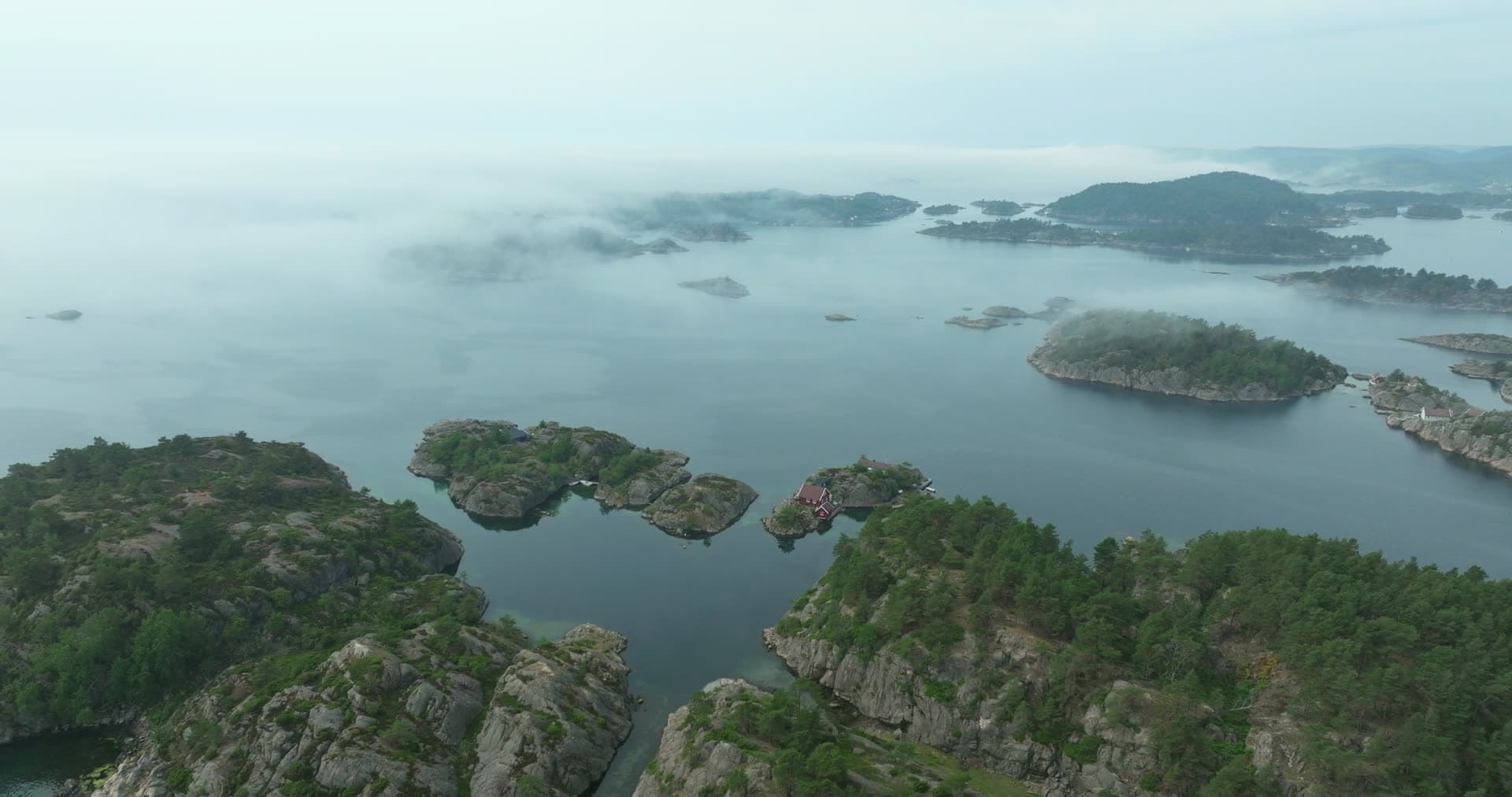 Red cabin on a rocky islet in low fog, Høllen, Norway