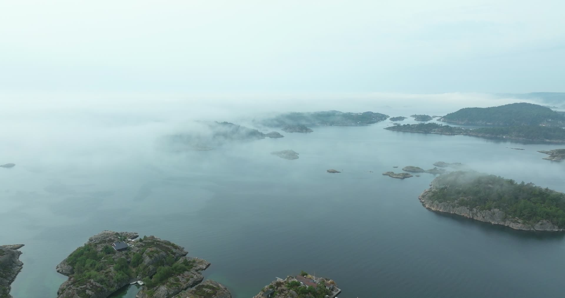 Sea fog drifting over rocky islets and cabins, Høllen, Norway