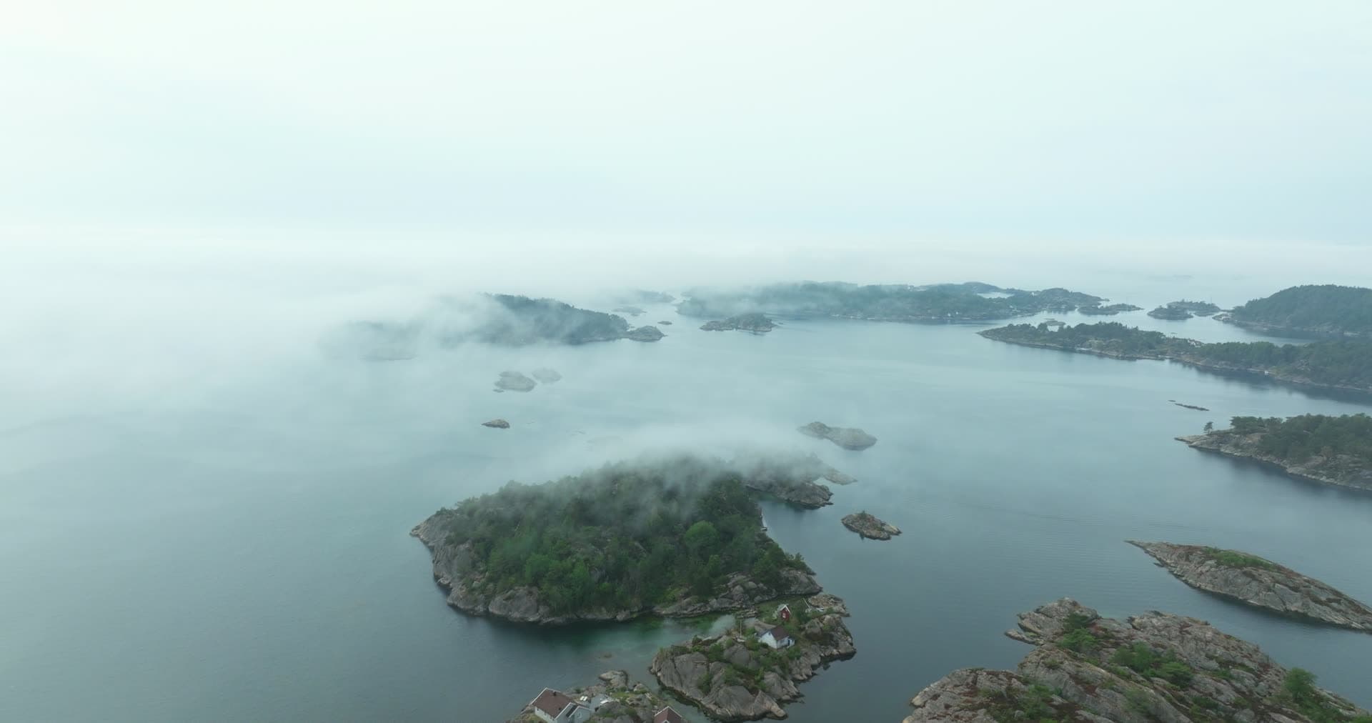 Fog drifting over rocky skerries and cabins, Høllen, Norway