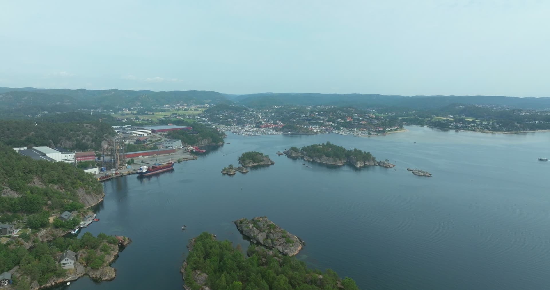 Cargo ship at industrial quay past rocky islets, Høllen, Norway