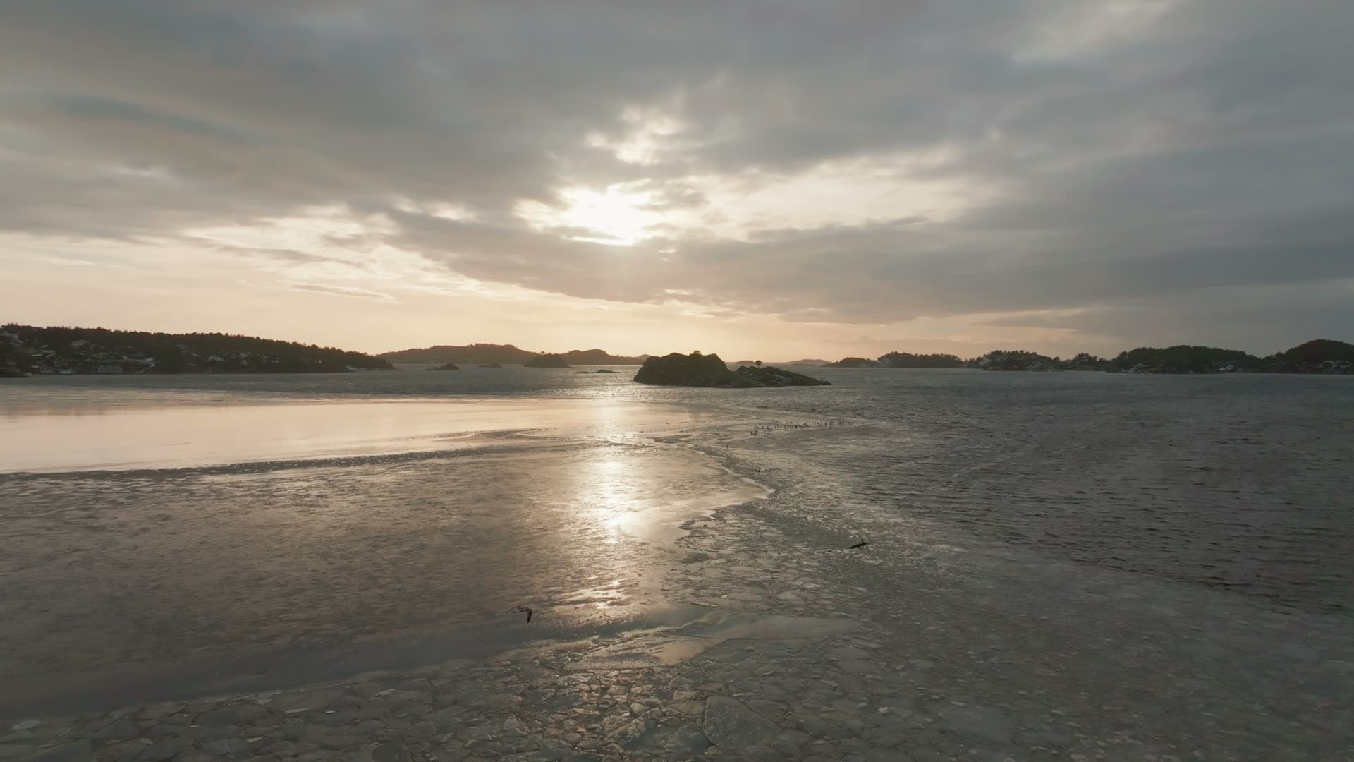 Sun glare on ice-covered fjord and islet, Høllen, Norway