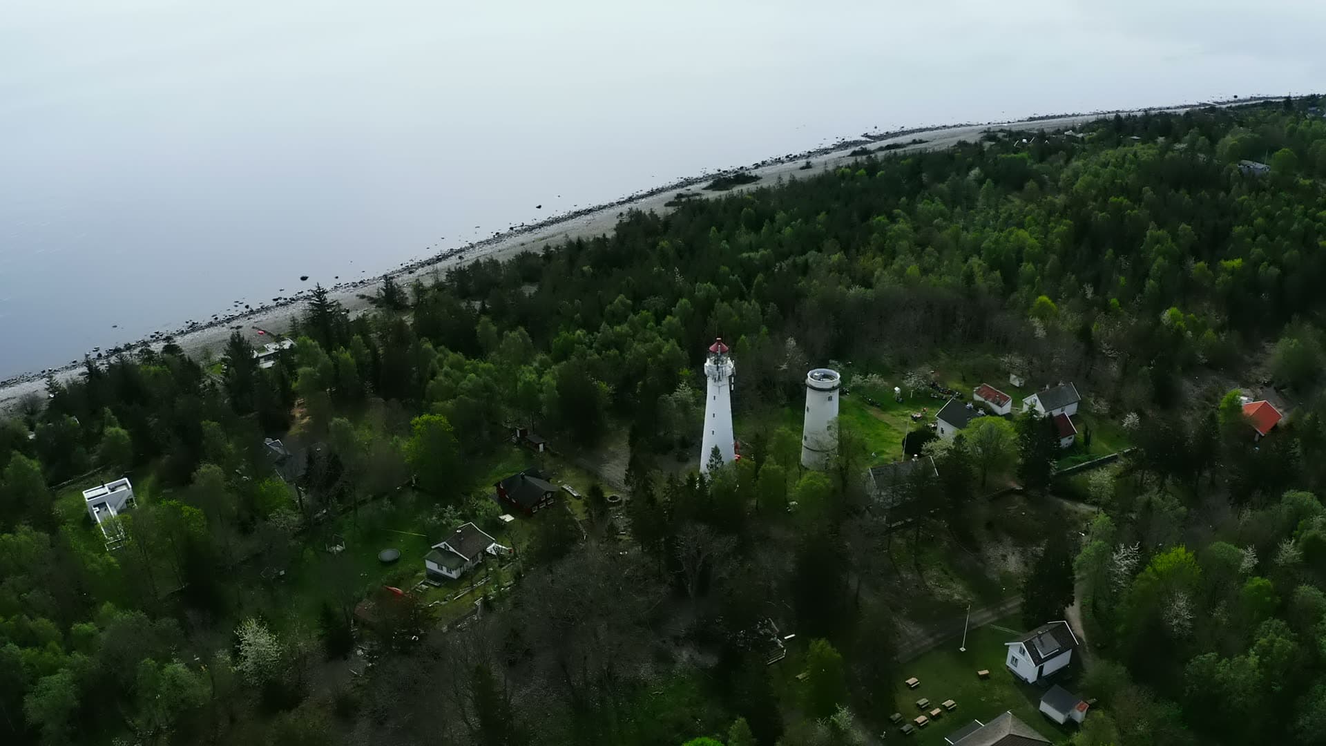 Two lighthouse towers above pine woods and stony beach, Jomfruland, Norway