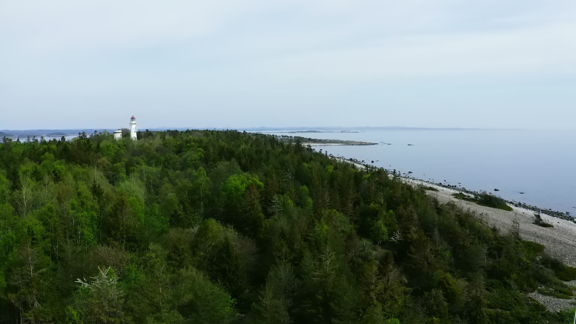 White lighthouse above forest and pebble beach, Jomfruland, Norway