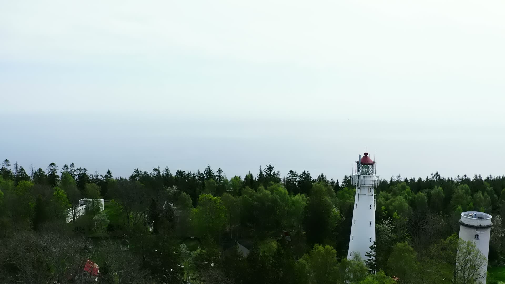 Red-topped lighthouse and old stone tower over forest, Jomfruland, Norway