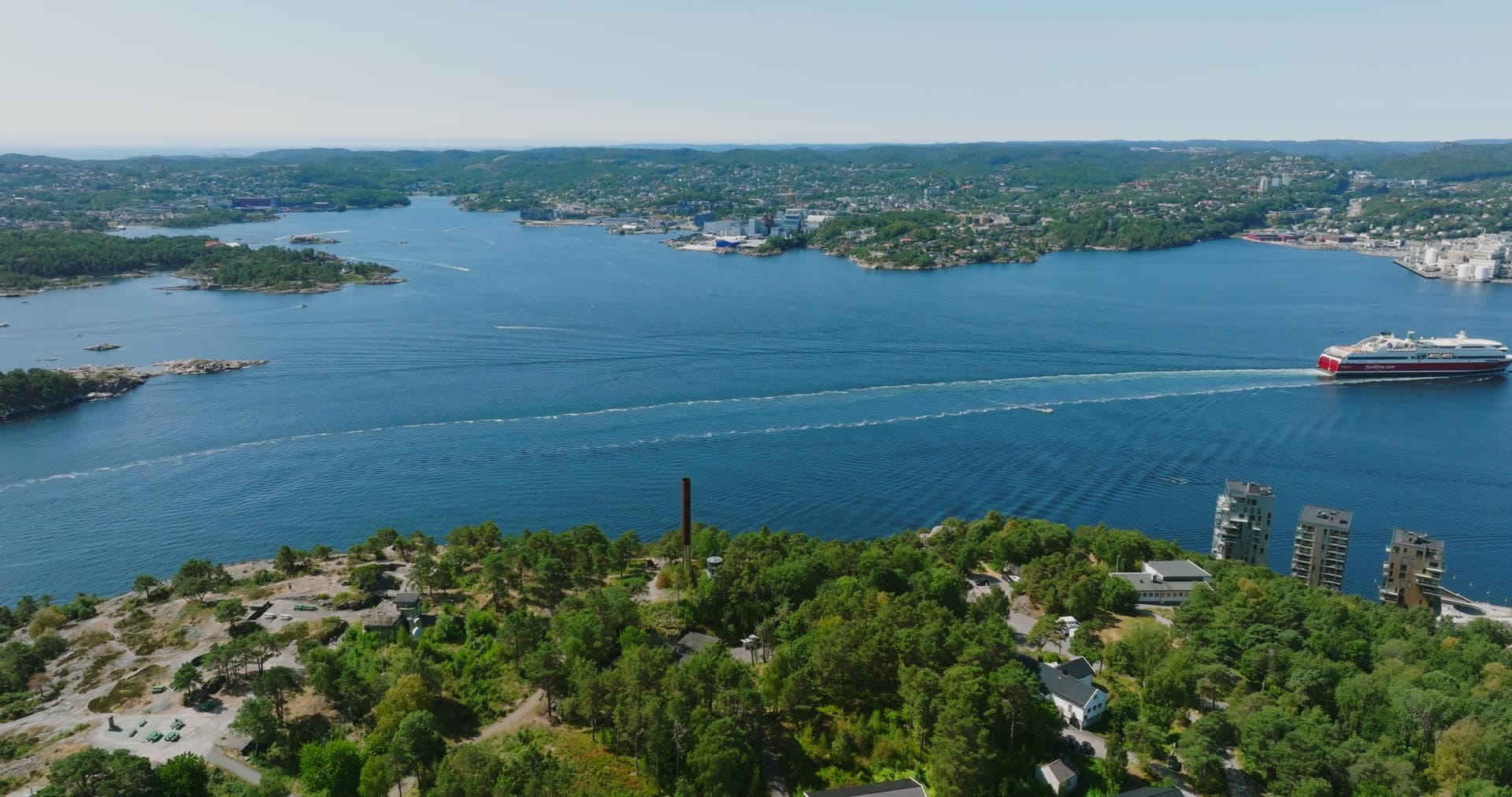 Red-hulled ferry under way past the chimney ridge, Kristiansand, Norway