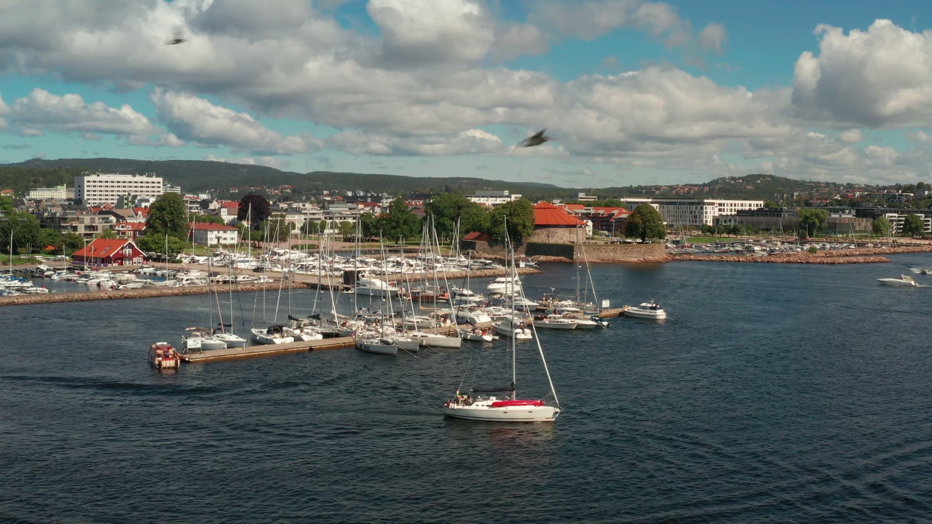Red-hulled deck sailboat motoring out, Kristiansand, Norway